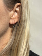 Model wearing Thalken 14k gold 12mm hoop earring with a small marquise black spinel drop in the first piercing, and a 10mm hoop with a small marquise drop in the second piercing