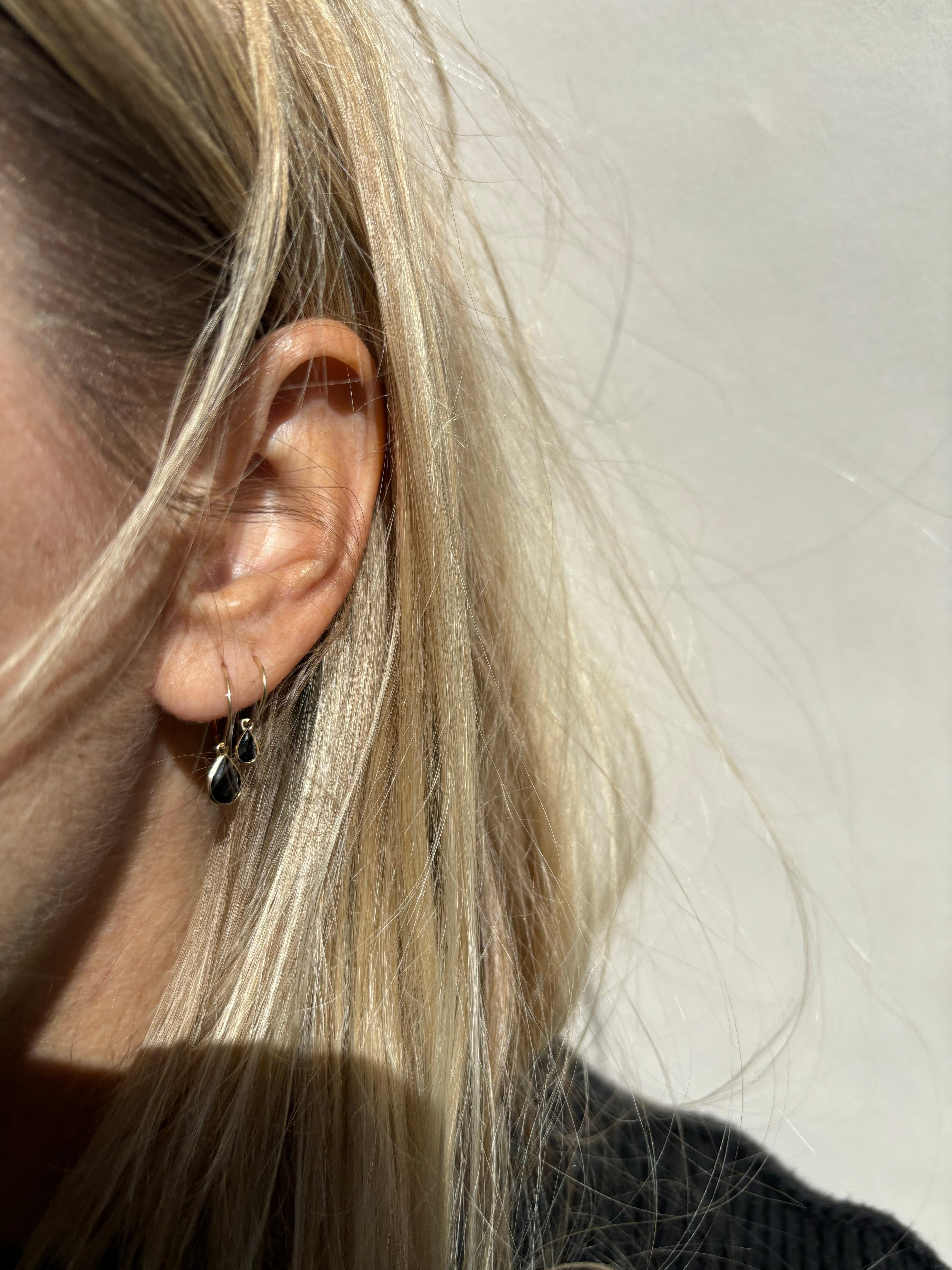 Model wearing Thalken 14k gold 12mm hoop earring with a large pear-shaped black spinel drop in the first piercing, and a 10mm hoop with a small pear drop in the second piercing