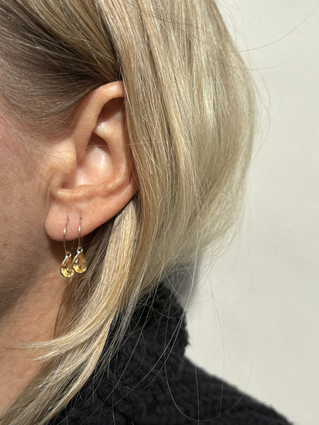 Close-up of model wearing Thalken 14k solid gold 12mm hoop earring with a large pear-shaped citrine drop in the first ear piercing, paired with a 10mm hoop and large pear-shaped citrine drop in the second ear piercing, highlighting elegant fine jewelry