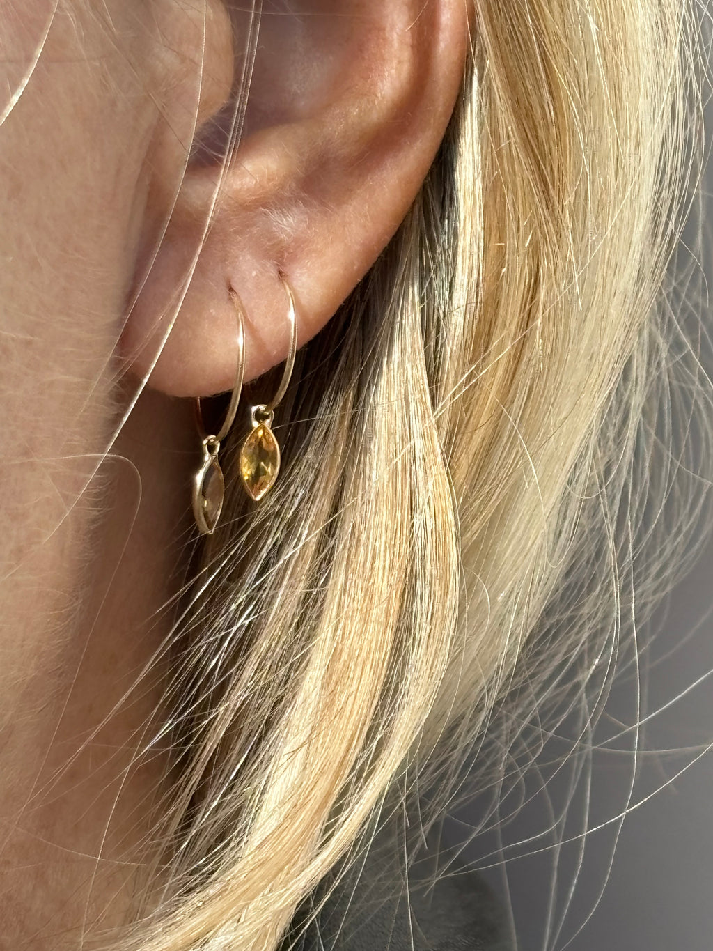 Close-up of model wearing Thalken 14k solid gold 12mm hoop earring with a small marquise-shaped citrine drop in the first ear piercing, and a 10mm hoop with a matching marquise citrine drop in the second piercing, showcasing minimalist fine jewelry styling
