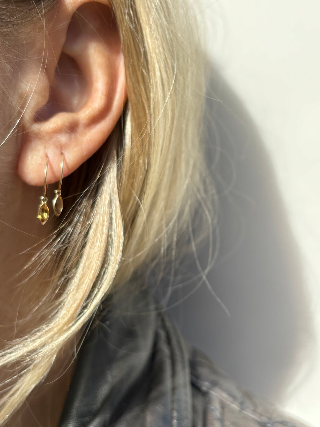Lifestyle action shot of a model wearing Thalken 14k solid gold 10mm hoop earring with a small marquise-shaped citrine drop, showcasing the earring’s movement and warm glow in natural light