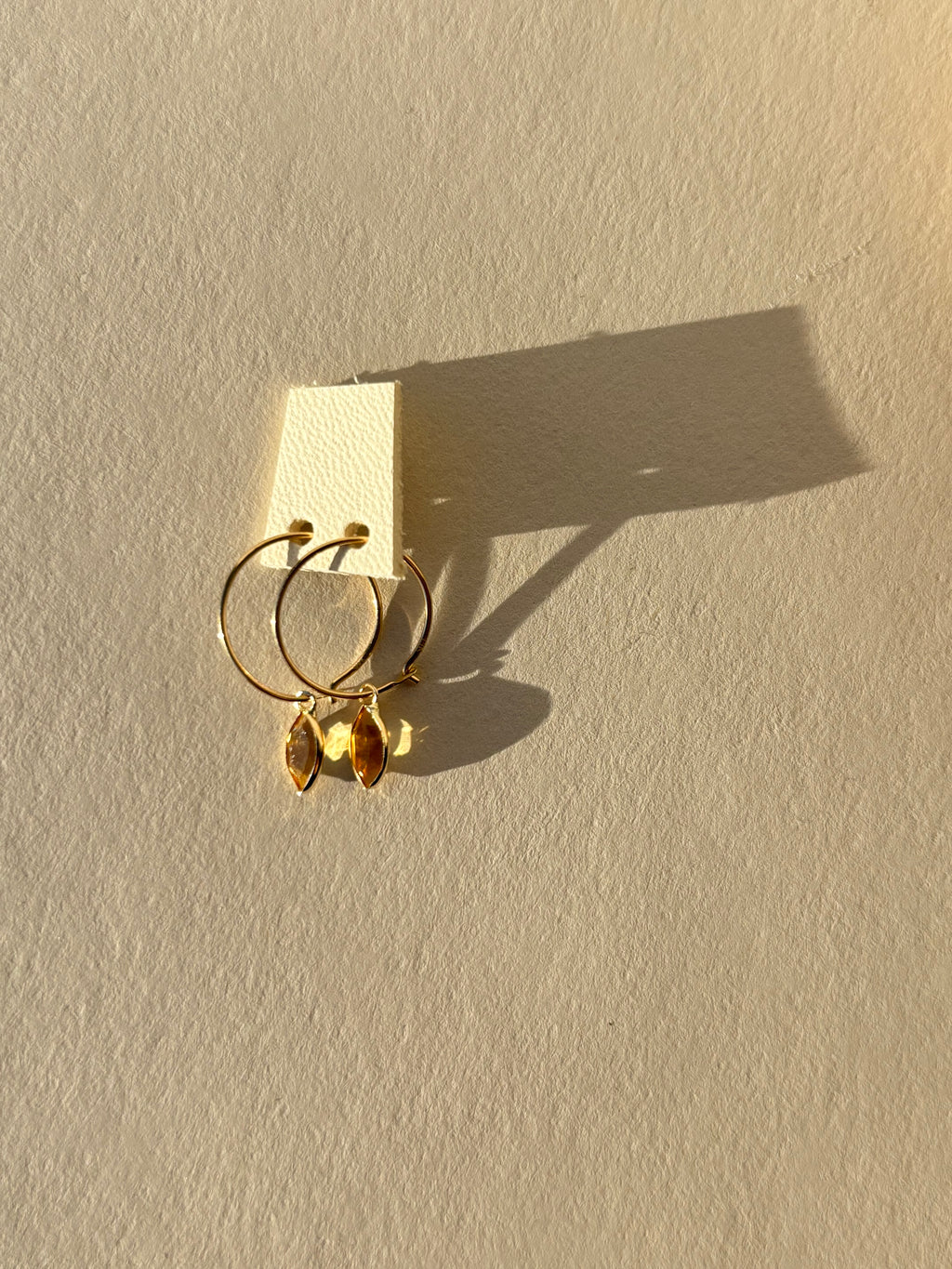 Pair of small marquise shaped 14k solid gold bezeled charms on 14k solid gold 12mm hoop earrings on white leather earring swatch