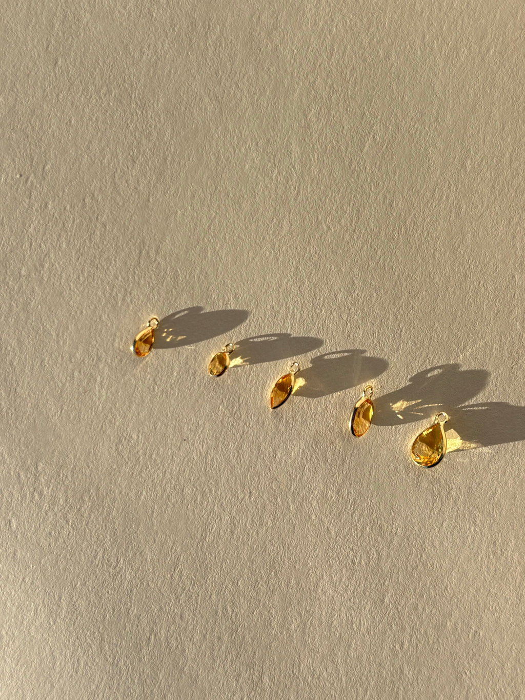 Assortment of Thalken 14k solid gold single drop earring charms in natural citrine, featuring pear, marquise, and oval shapes, displayed unattached to hoops for customizable earring styling
