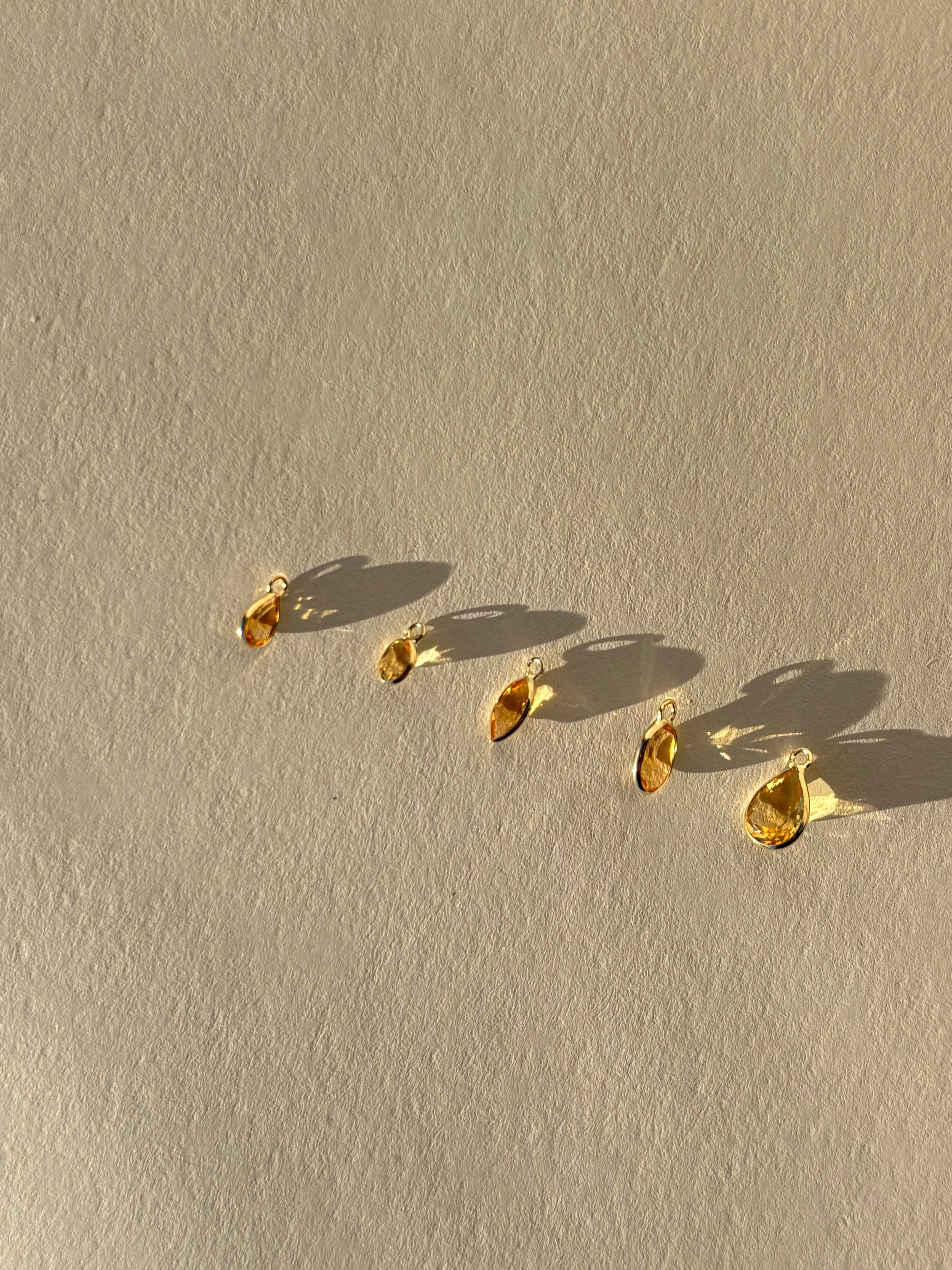 Assortment of Thalken 14k solid gold single drop earring charms in natural citrine, featuring pear, marquise, and oval shapes, displayed unattached to hoops for customizable earring styling