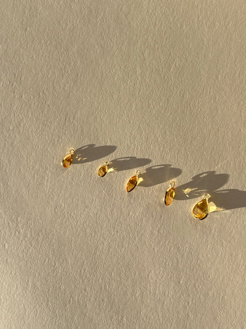 Assortment of Thalken 14k solid gold single drop earring charms in natural citrine, featuring pear, marquise, and oval shapes, displayed unattached to hoops for customizable earring styling