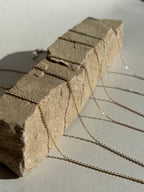 Close-up of three delicate chains: yellow gold-filled 1.3mm, rose gold-filled 1.1mm, and sterling silver 1.1mm, artfully arranged on a rock