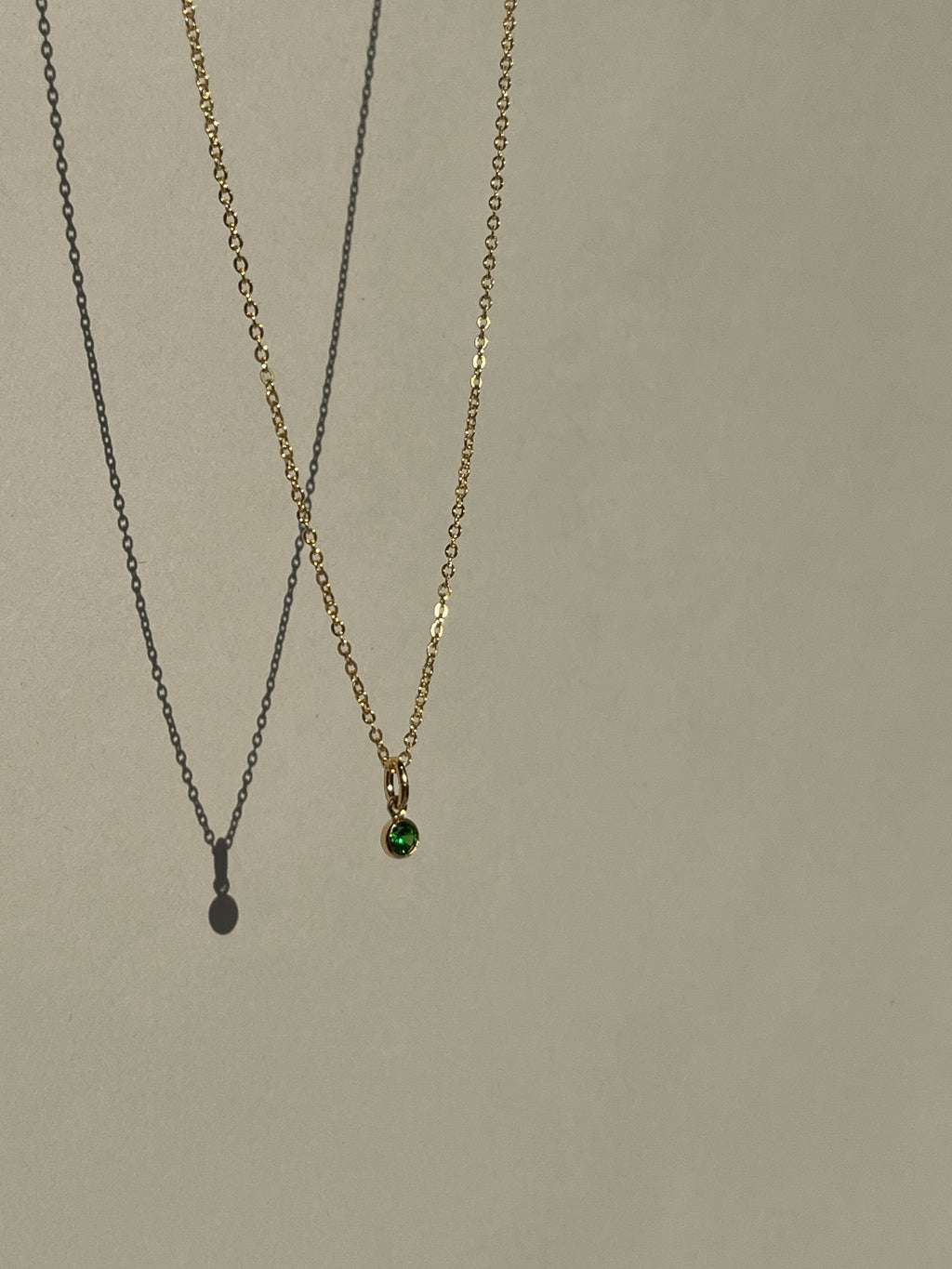 Green May birthstone cubic zirconia charm suspended on a dainty gold-filled chain against a natural outdoor background