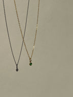 Green May birthstone cubic zirconia charm suspended on a dainty gold-filled chain against a natural outdoor background
