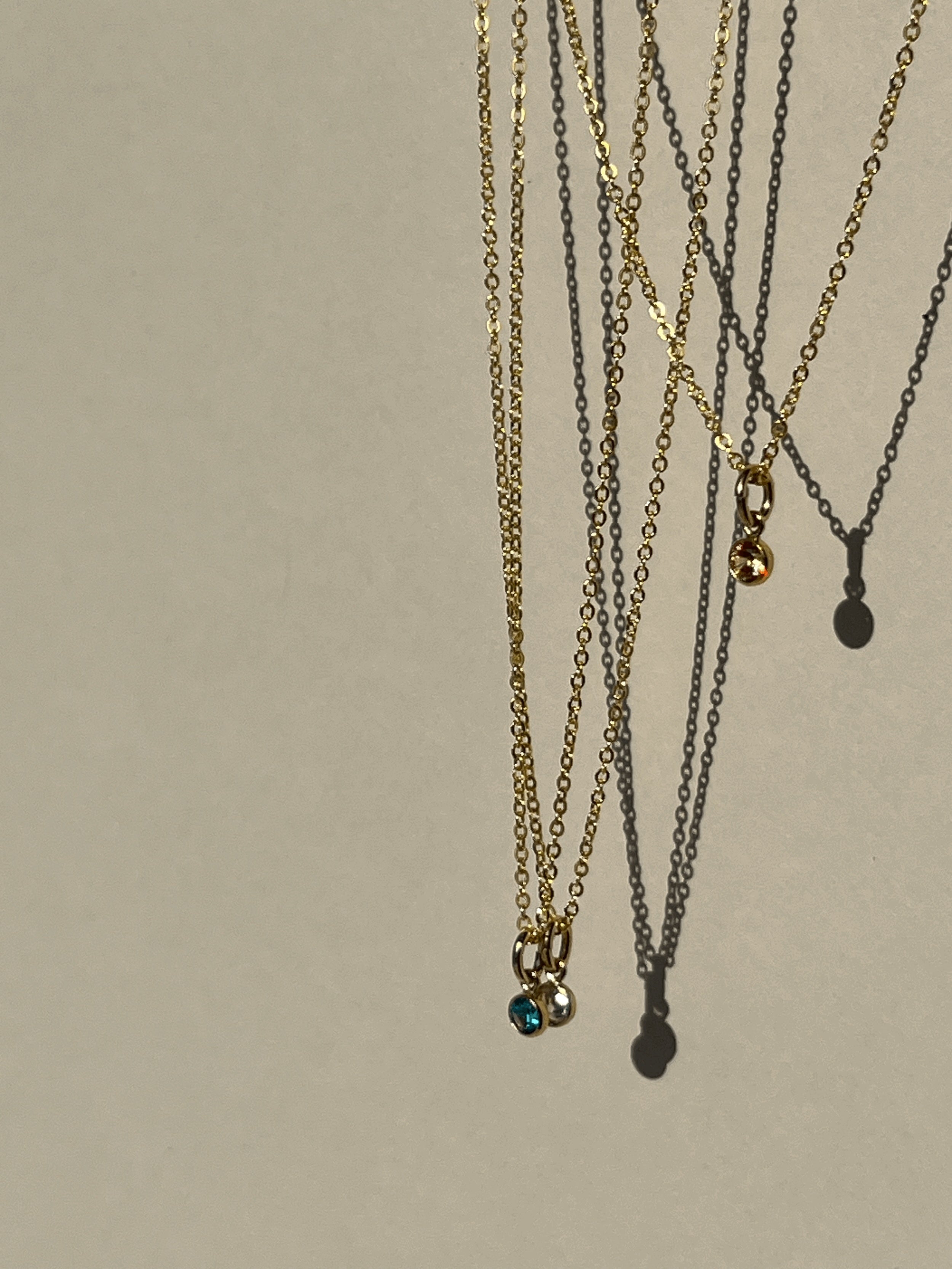 Blue, peach, and clear cubic zirconia birthstone charms on dainty gold-filled chains, suspended in mid-air against a natural background