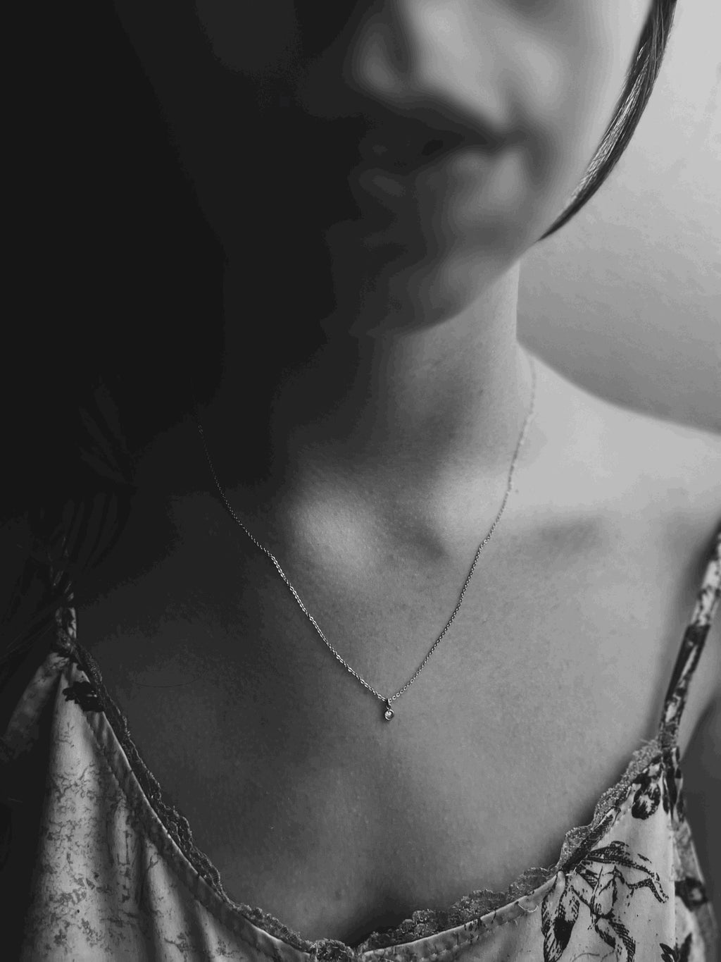 Black and white moody photo of model wearing Thalken’s dainty sterling silver birthstone necklace with a single 3mm bezel-set cubic zirconia charm