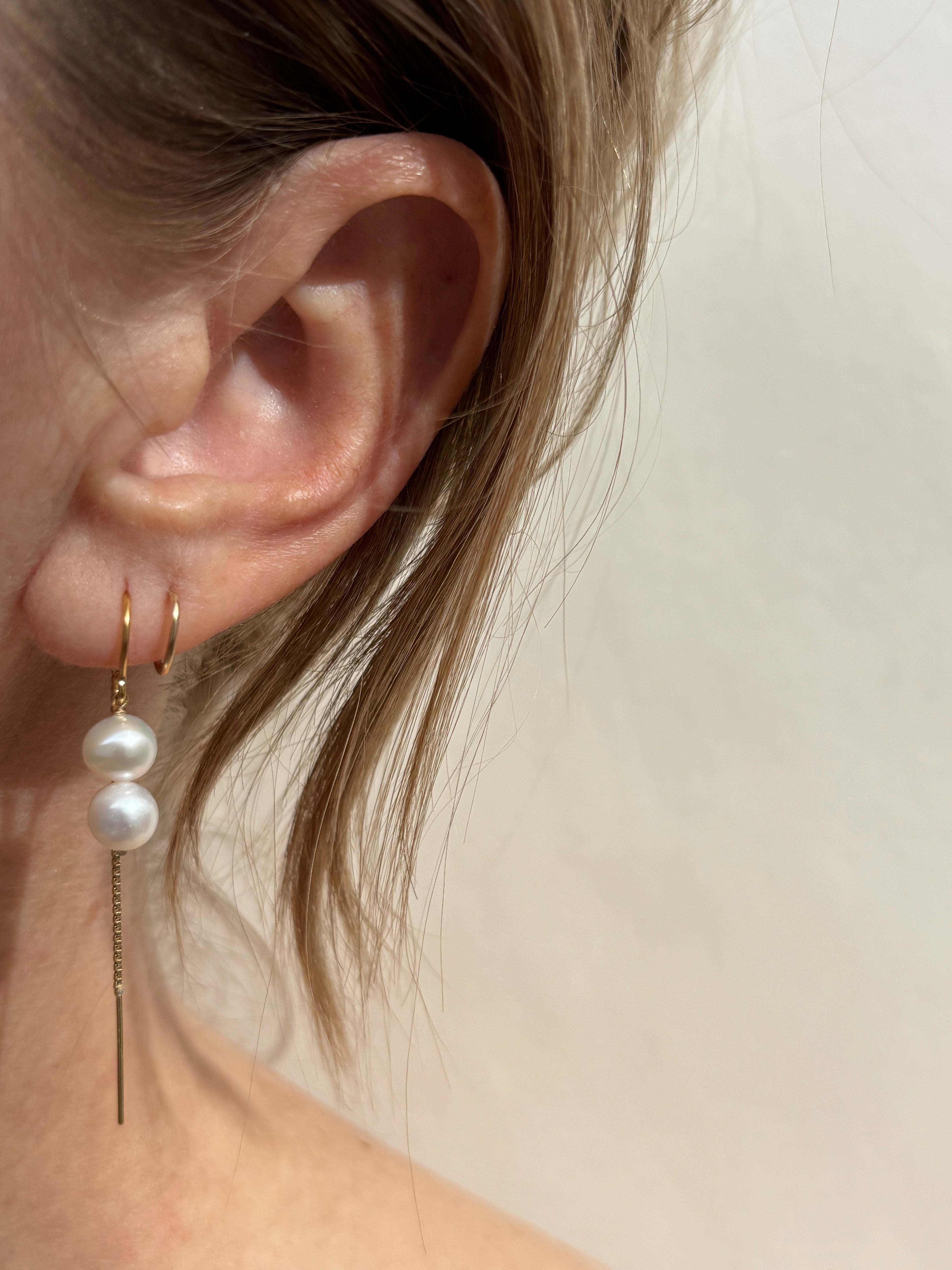 Double pearl threader earrings in first ear piercing on an ear with a tiny hoop in the second piercing 