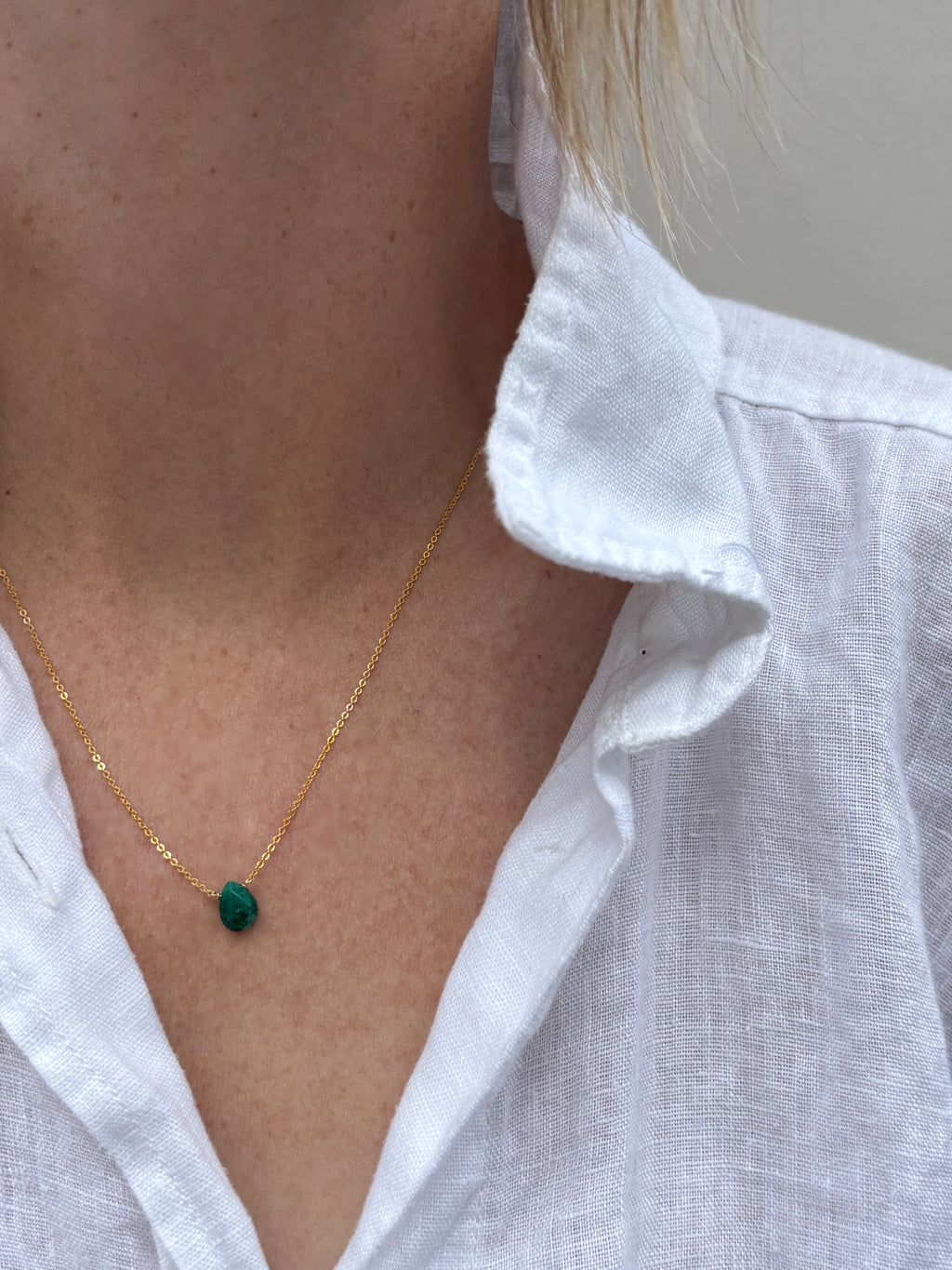 Close-up of model wearing dainty emerald drop necklace in white linen shirt