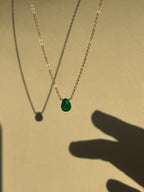 Thalken Emerald Drop Necklace with a green stone suspended in air, shadow of fingers reaching toward the necklace