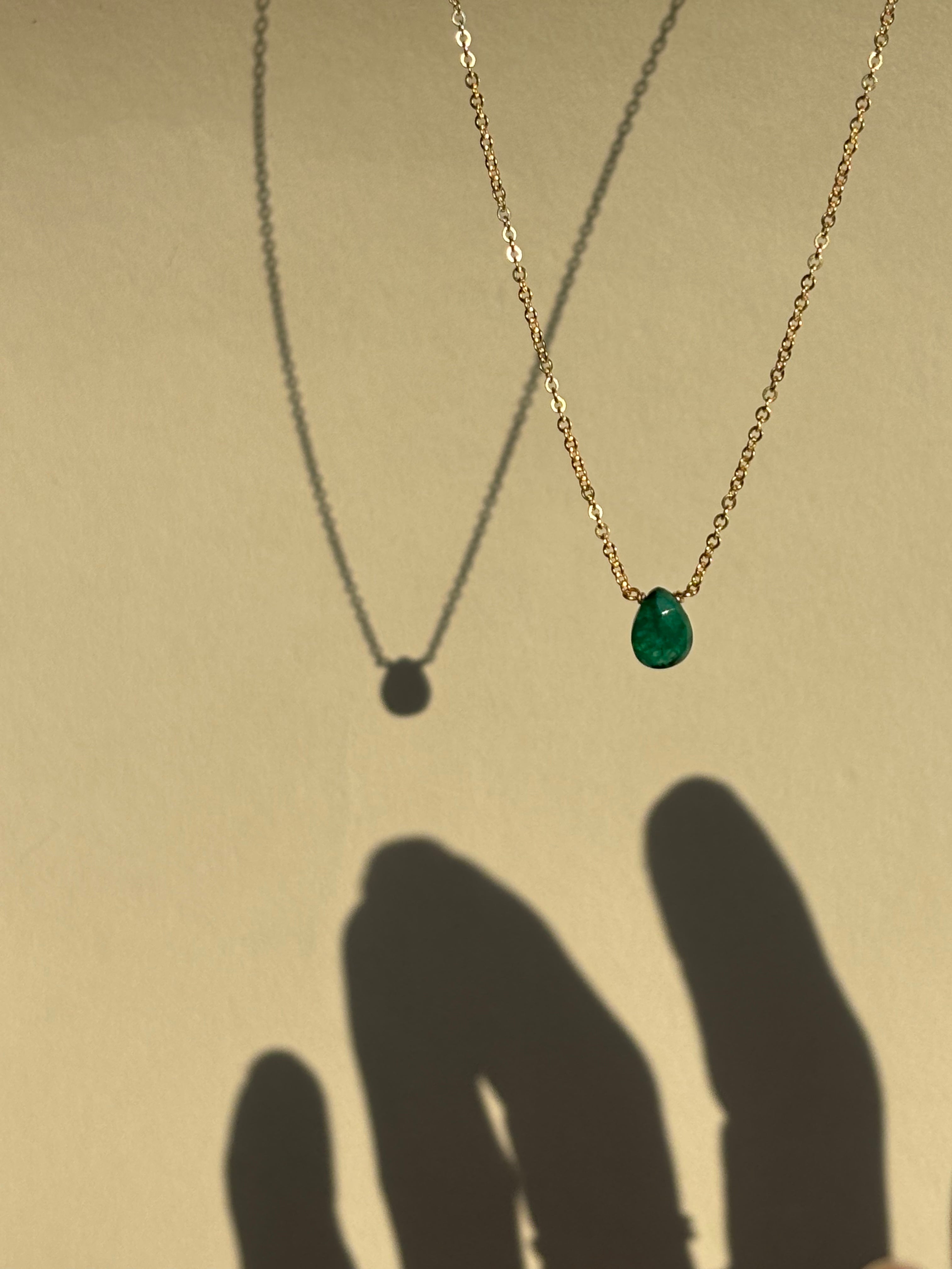 Green emerald stone necklace suspended in air, shadow of fingers reaching toward the necklace