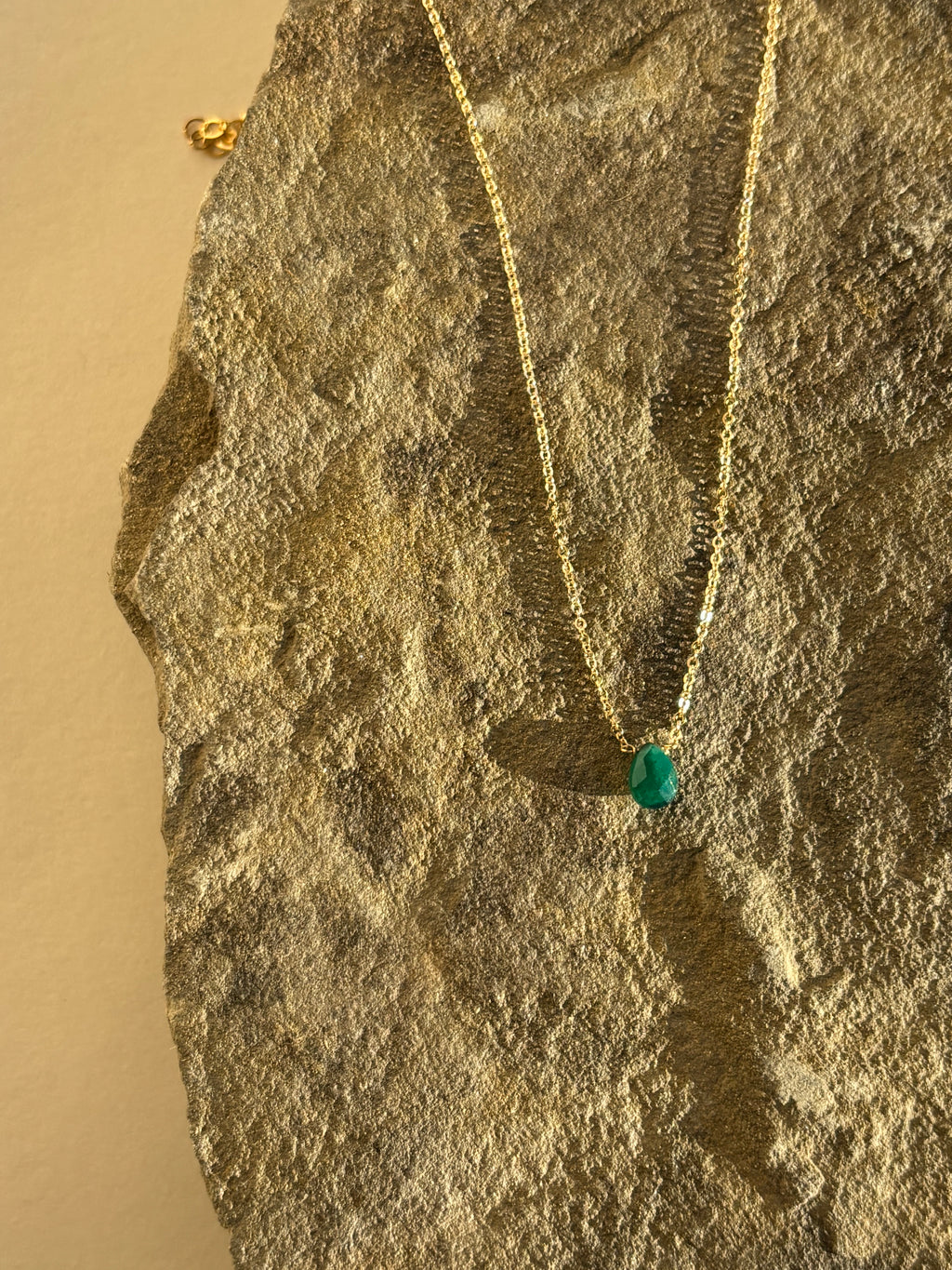 Thalken Emerald Drop Necklace with a green stone displayed on a natural rock