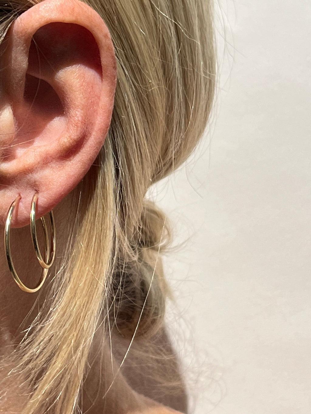 Model wearing 24mm gold-filled hoops in her first ear piercing and 20mm hoops in her second, displaying mid-size layering