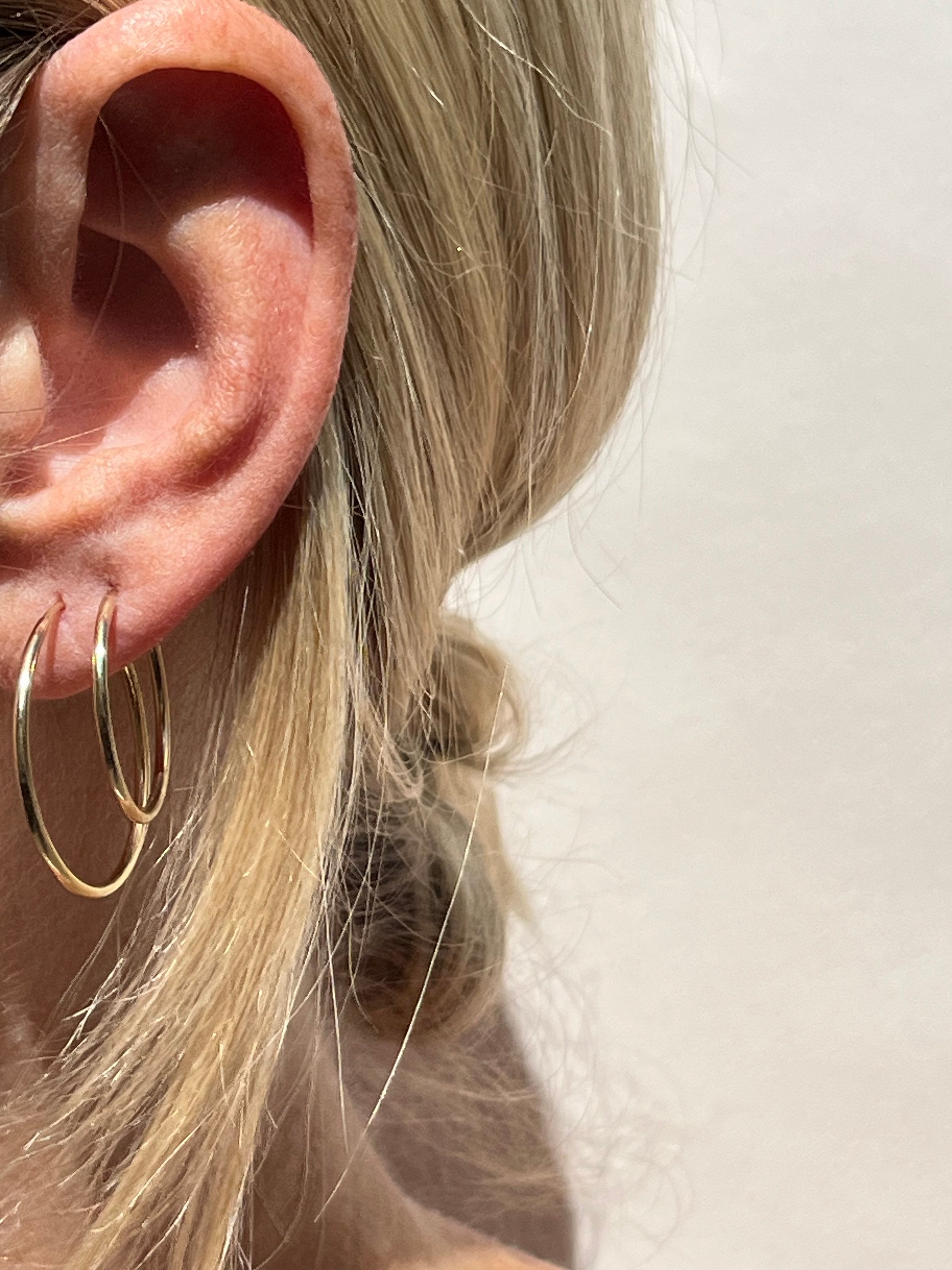 Model wearing 24mm gold-filled hoops in her first ear piercing and 20mm hoops in her second, displaying mid-size layering