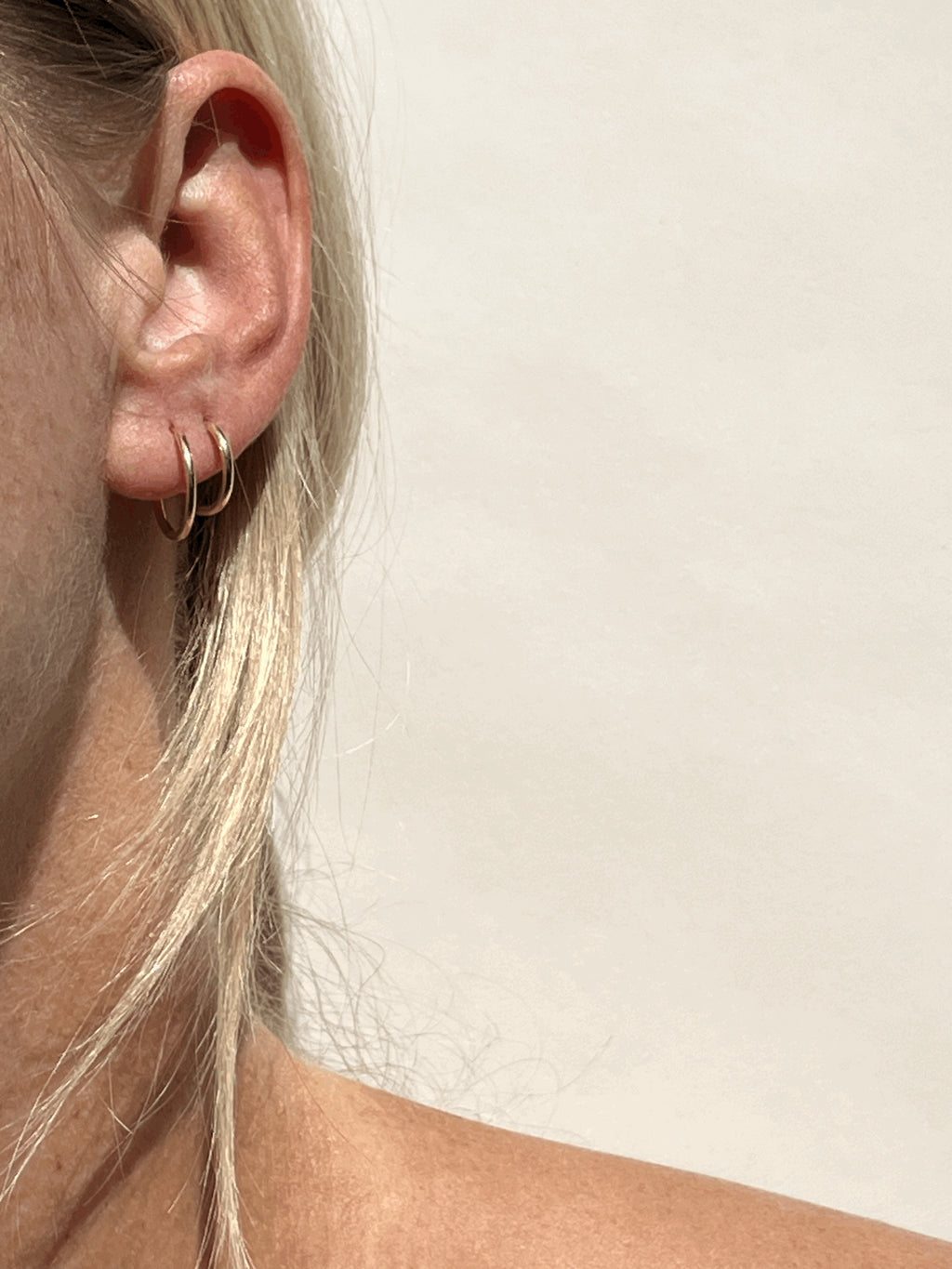Close-up of model wearing 14mm gold-filled hoops in her first piercing and 12mm hoops in her second, showing small hoop sizes worn together