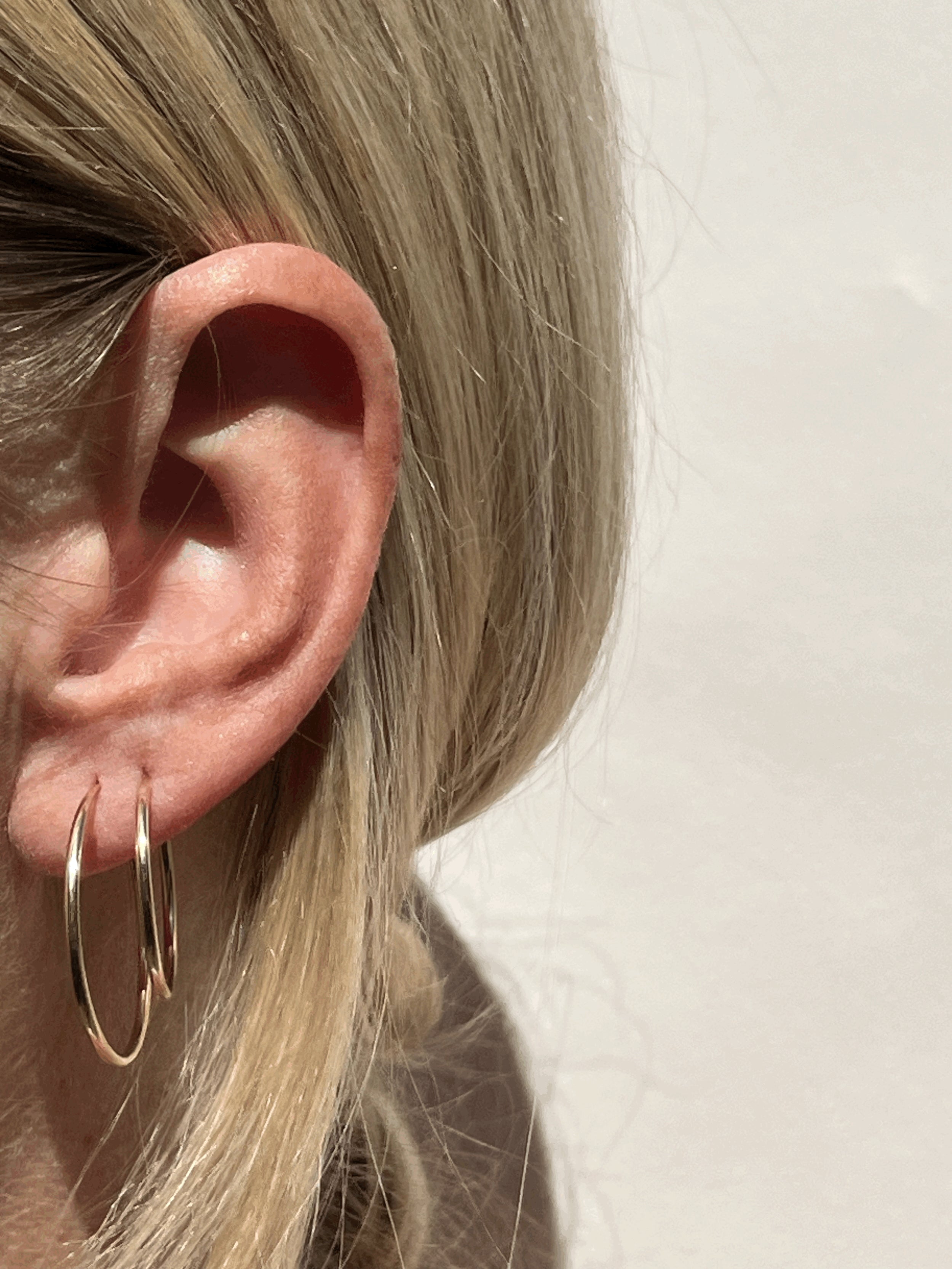 Side view of model wearing 24mm and 20mm gold-filled endless hoops in first and second earlobe piercings