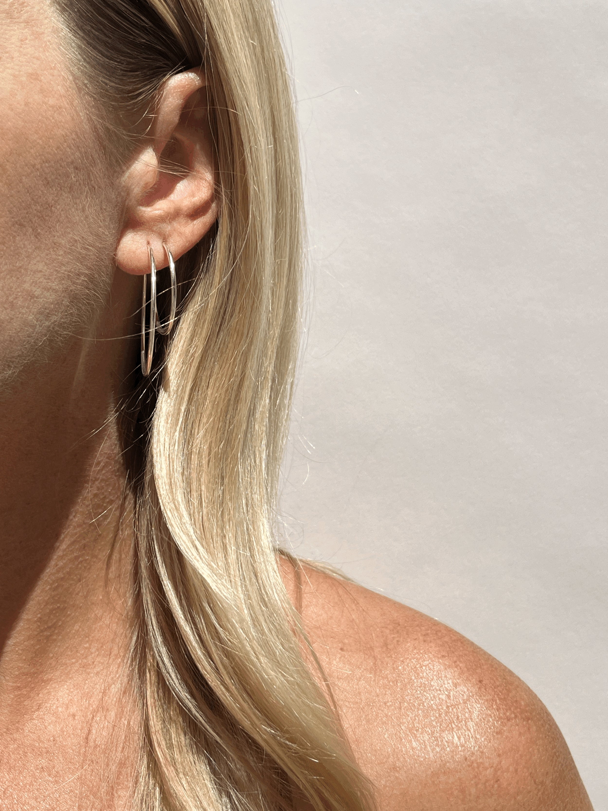 Model wearing 35mm sterling silver hoops in her first ear piercing and 24mm hoops in her second