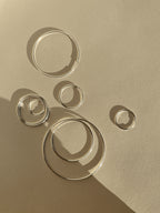 Artistic flat lay of all eleven sizes of sterling silver endless hoops arranged in a floating, bubble-like pattern on a soft background