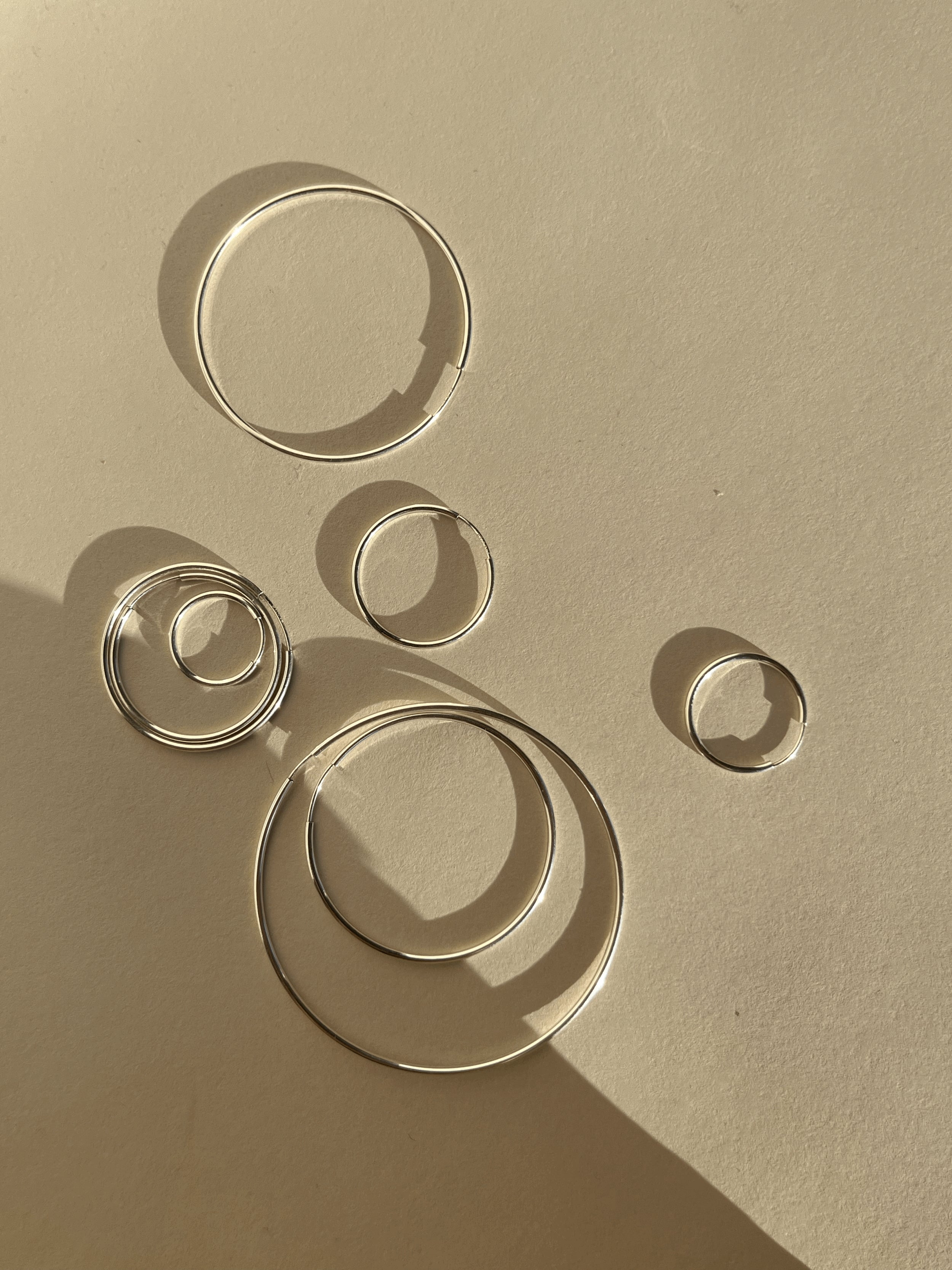 Artistic flat lay of all eleven sizes of sterling silver endless hoops arranged in a floating, bubble-like pattern on a soft background