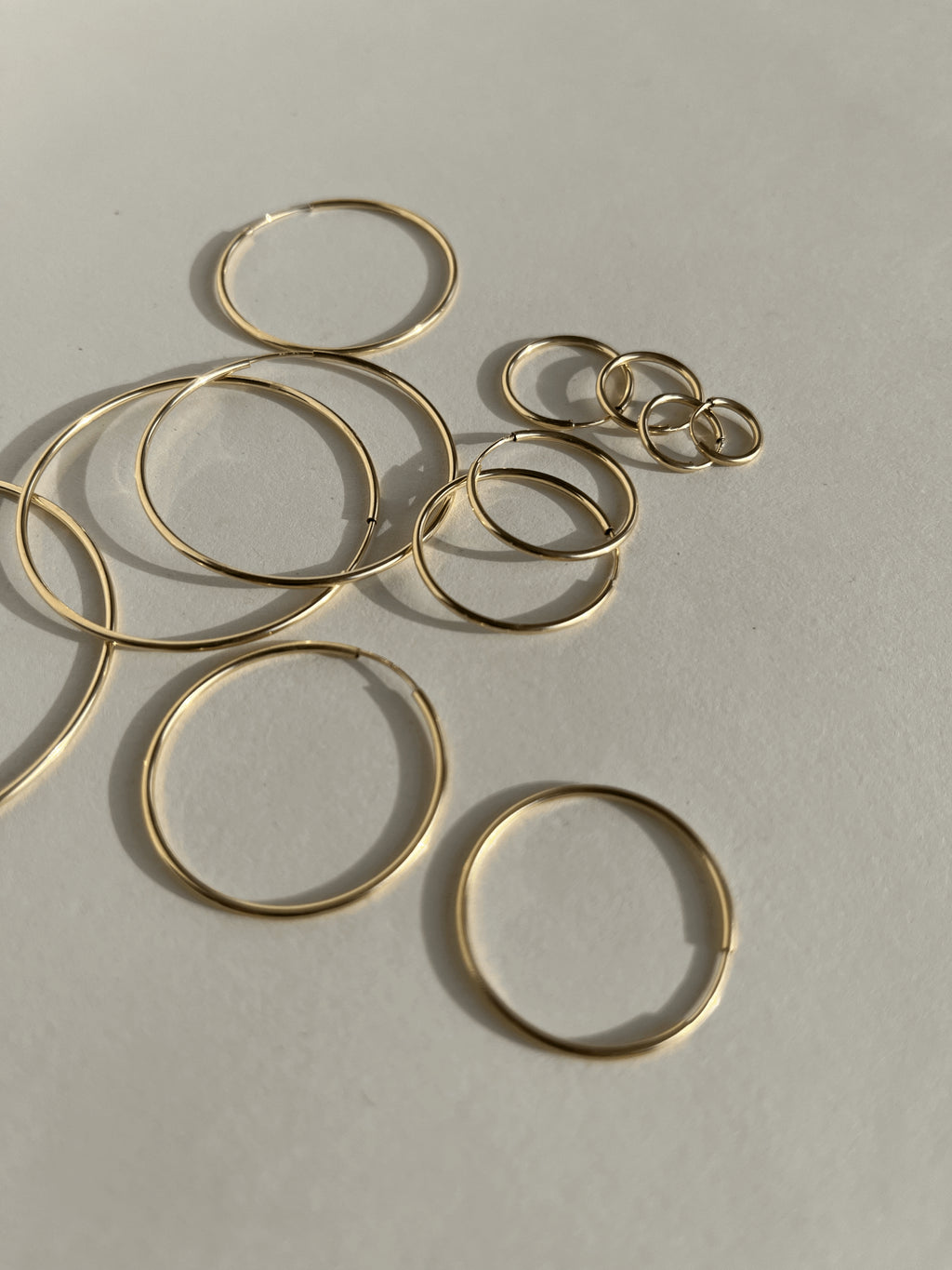 Artistic flat lay of all eleven sizes of gold-filled endless hoops arranged in a floating, bubble-like pattern, showcasing the full size range from 12mm to 50mm