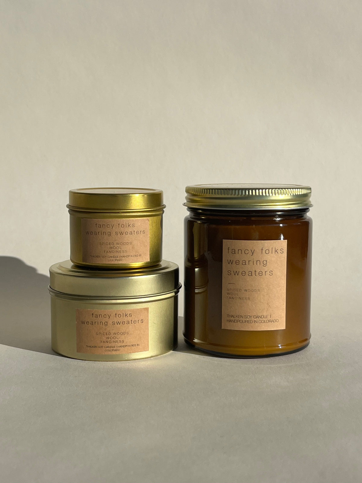 Three Thalken Fancy Folks Wearing Sweaters candles in small and medium gold tins and a large brown glass jar