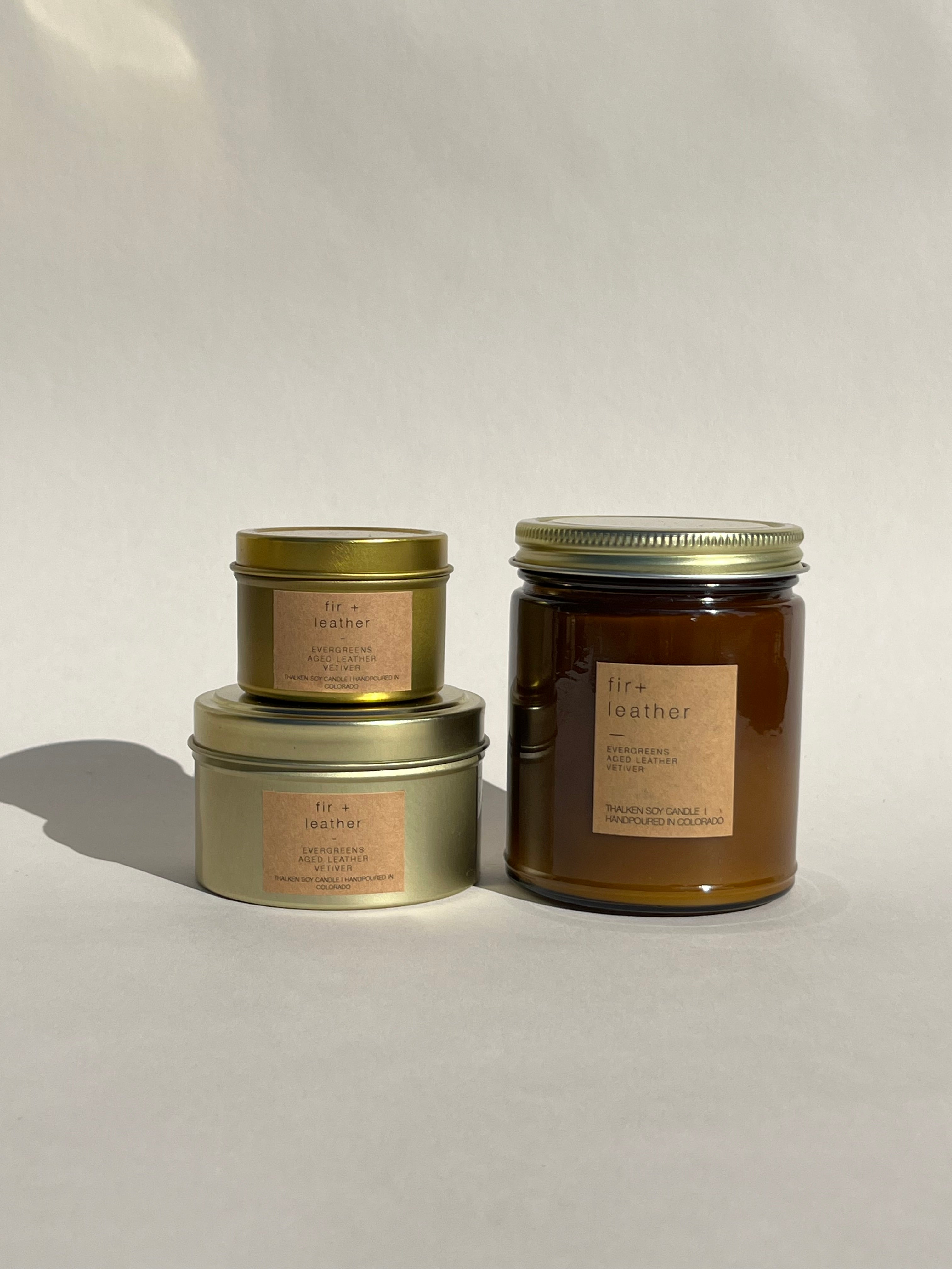 Thalken Fir and Leather candle in three containers: small gold tin, medium gold tin, and large brown glass jar