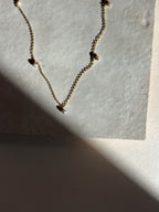 Close-up of the fog-toned freshwater pearl Whisper raindrop necklace on an organic tile surface with warm, moody lighting showing pearl spacing and fixed pearl details.