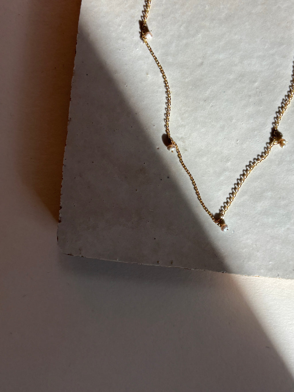 Close-up of the fog-toned freshwater pearl Whisper raindrop necklace on an organic tile surface with warm, moody lighting showing pearl spacing and fixed pearl details.