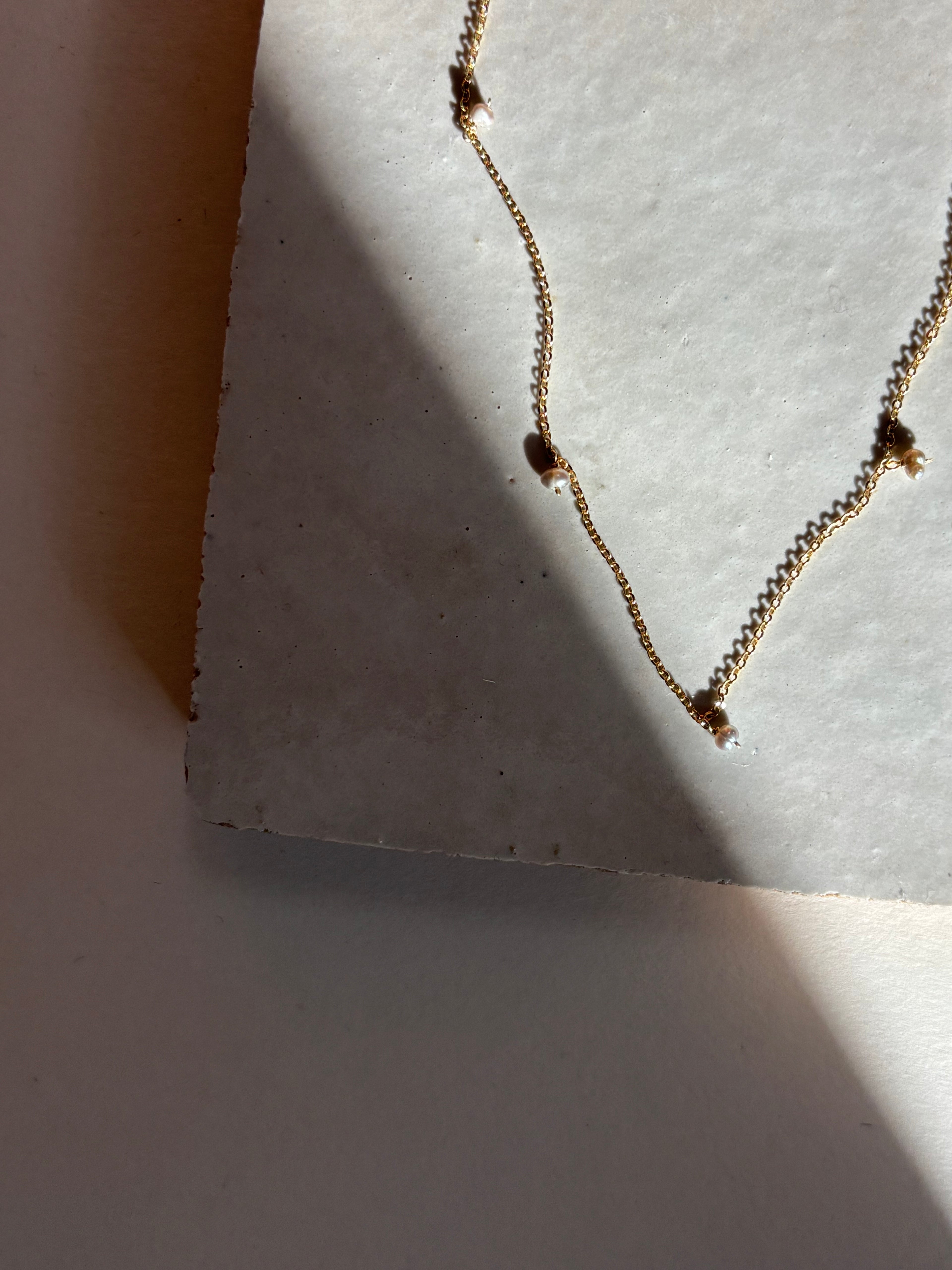 Close-up of the fog-toned freshwater pearl Whisper raindrop necklace on an organic tile surface with warm, moody lighting showing pearl spacing and fixed pearl details.