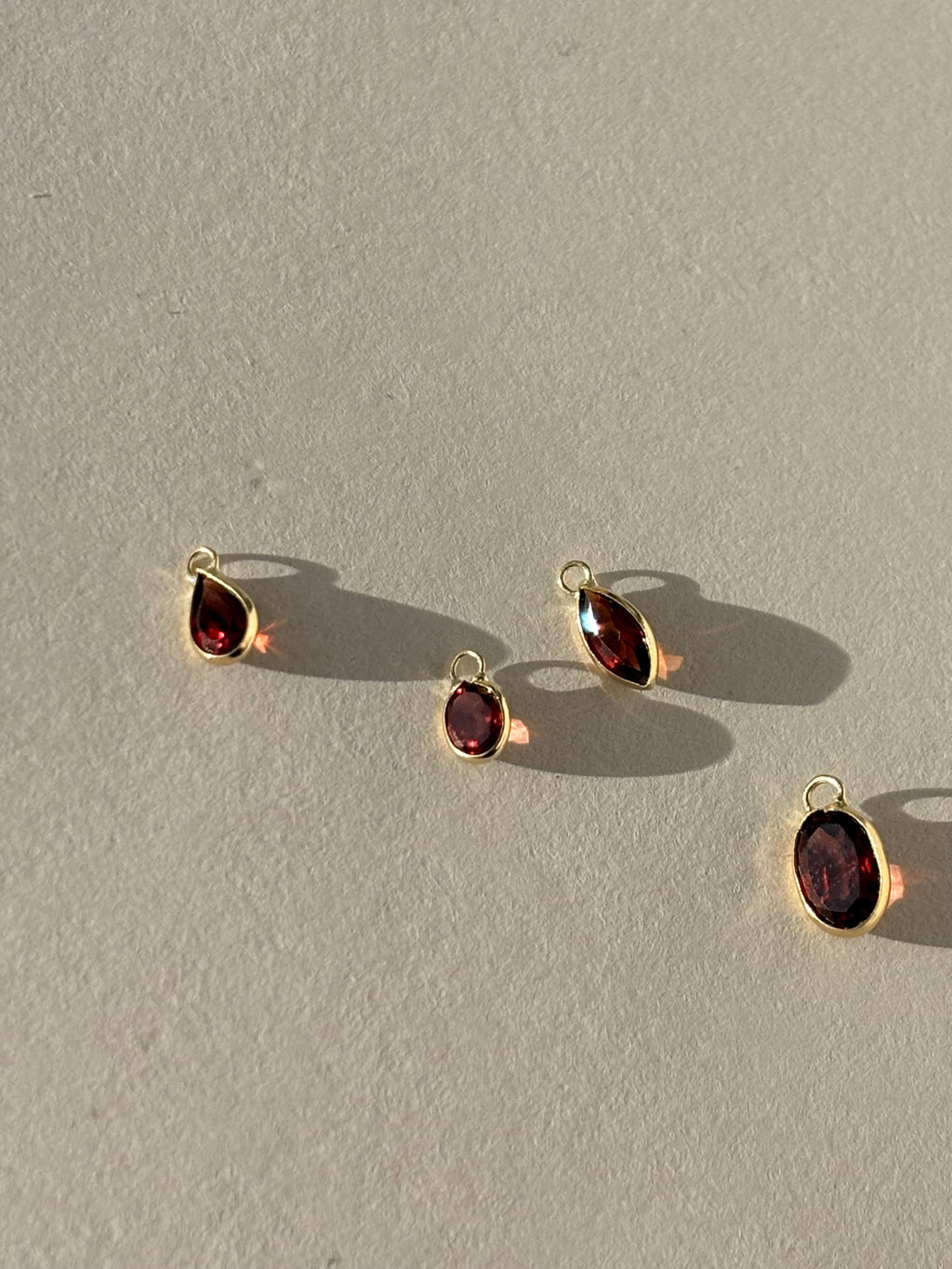 Close-up of Collection of Thalken 14k solid gold garnet drop charms in assorted sizes and shapes, shown unattached to hoop earrings for customizable gemstone jewelry styling