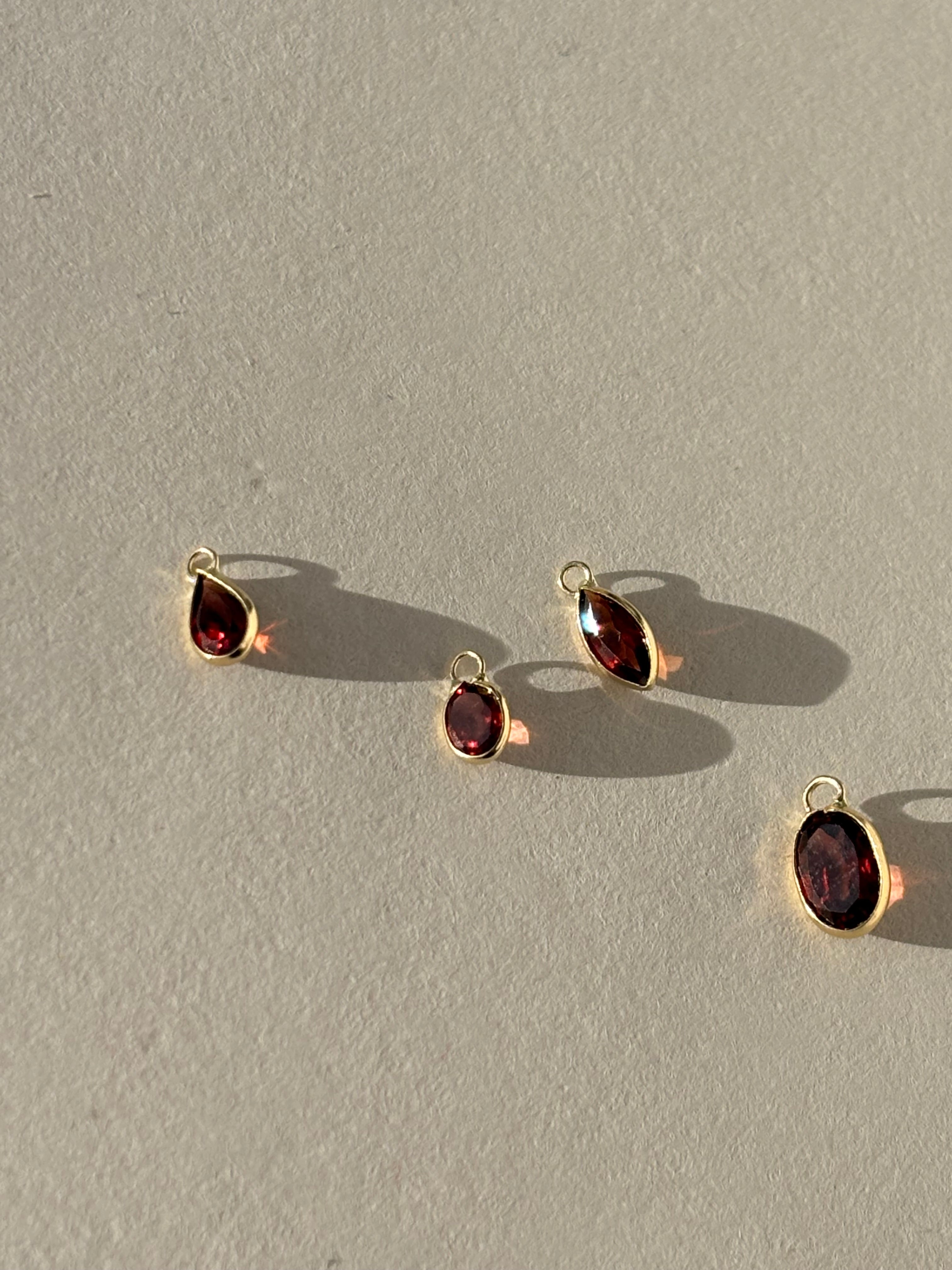 Close-up of Collection of Thalken 14k solid gold garnet drop charms in assorted sizes and shapes, shown unattached to hoop earrings for customizable gemstone jewelry styling