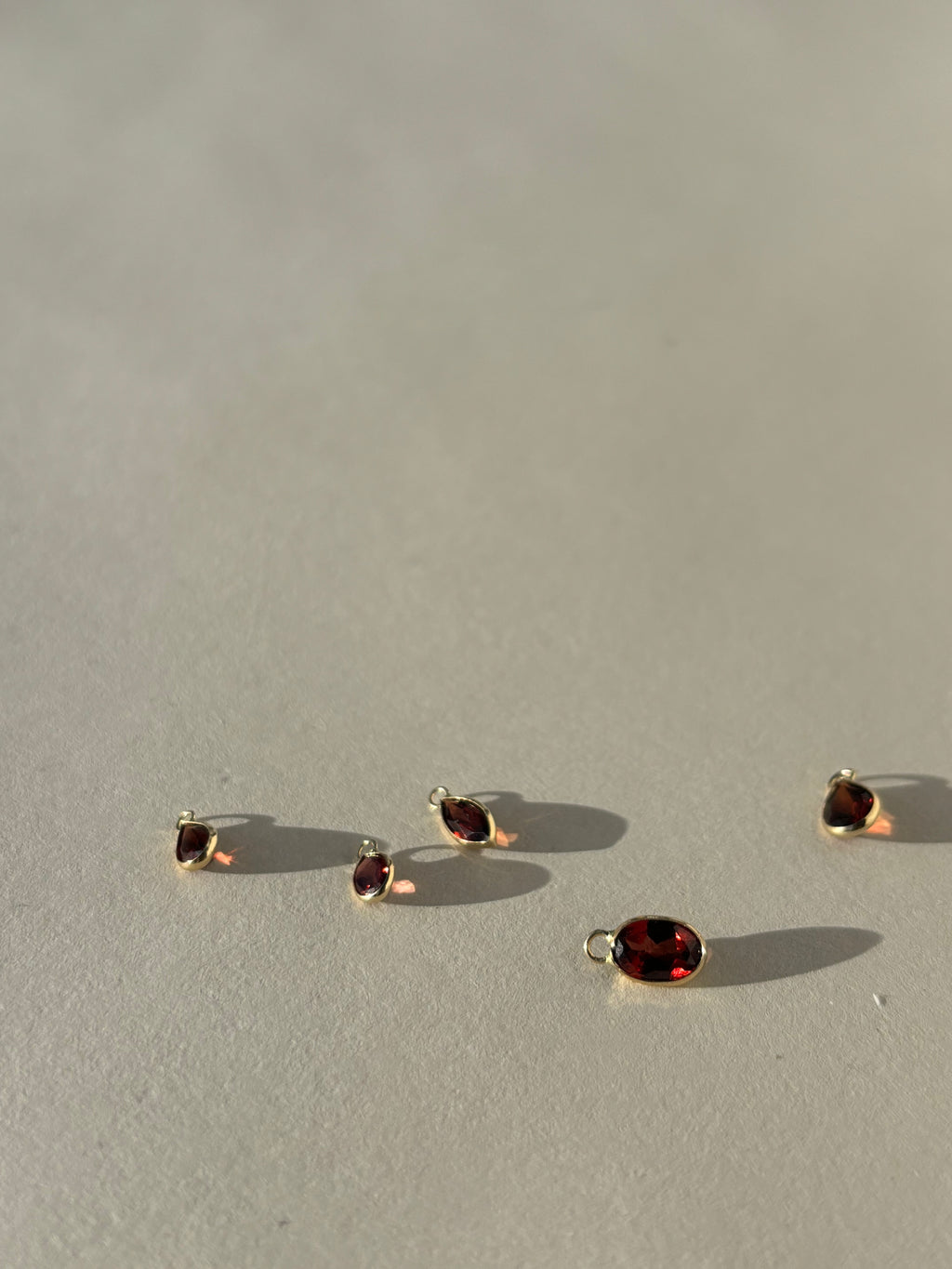 Thalken 14k gold garnet earring charms in pear, marquise, and oval shapes, displayed unattached to hoops for versatile mix-and-match styling