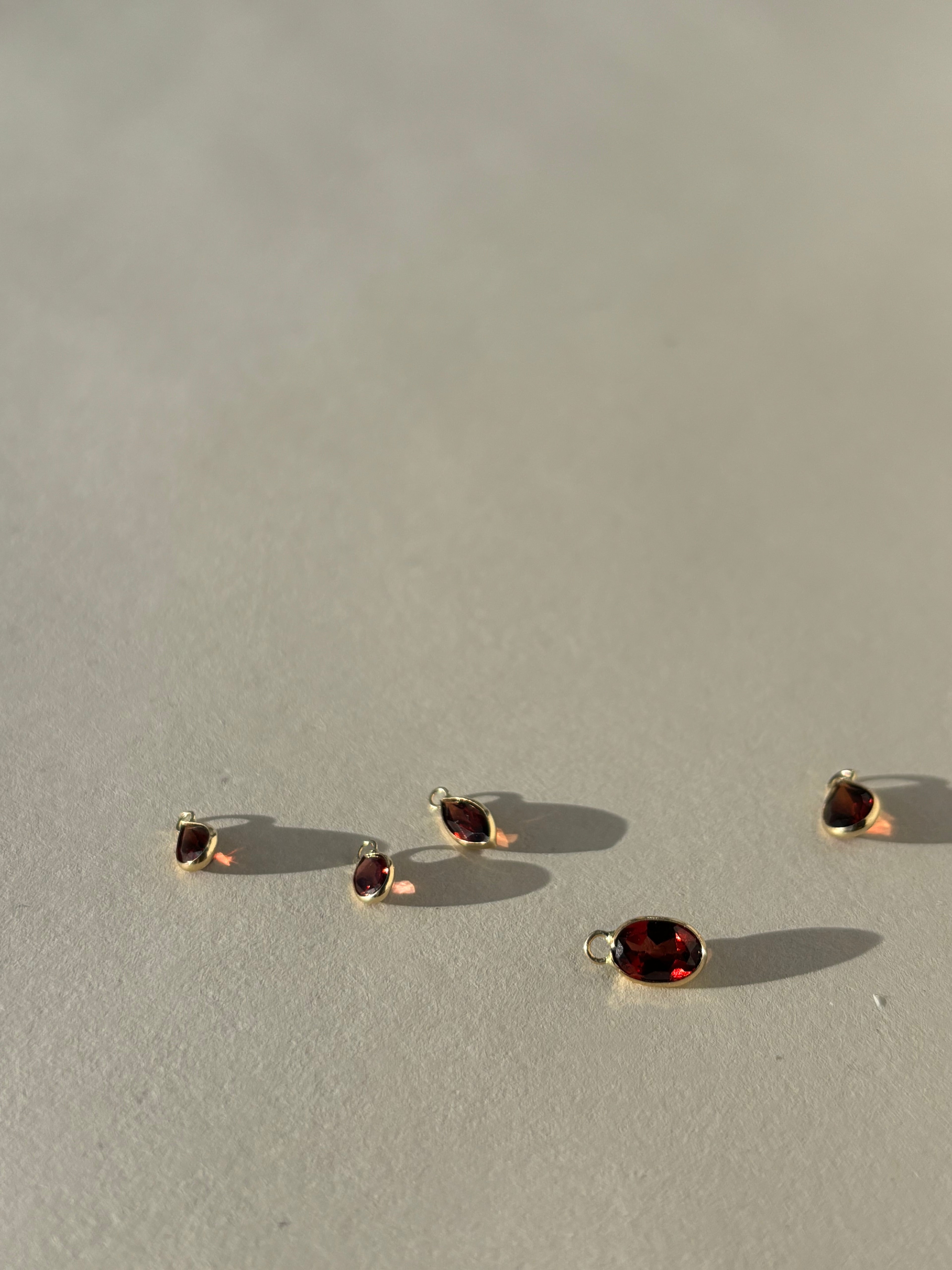 Thalken 14k gold garnet earring charms in pear, marquise, and oval shapes, displayed unattached to hoops for versatile mix-and-match styling