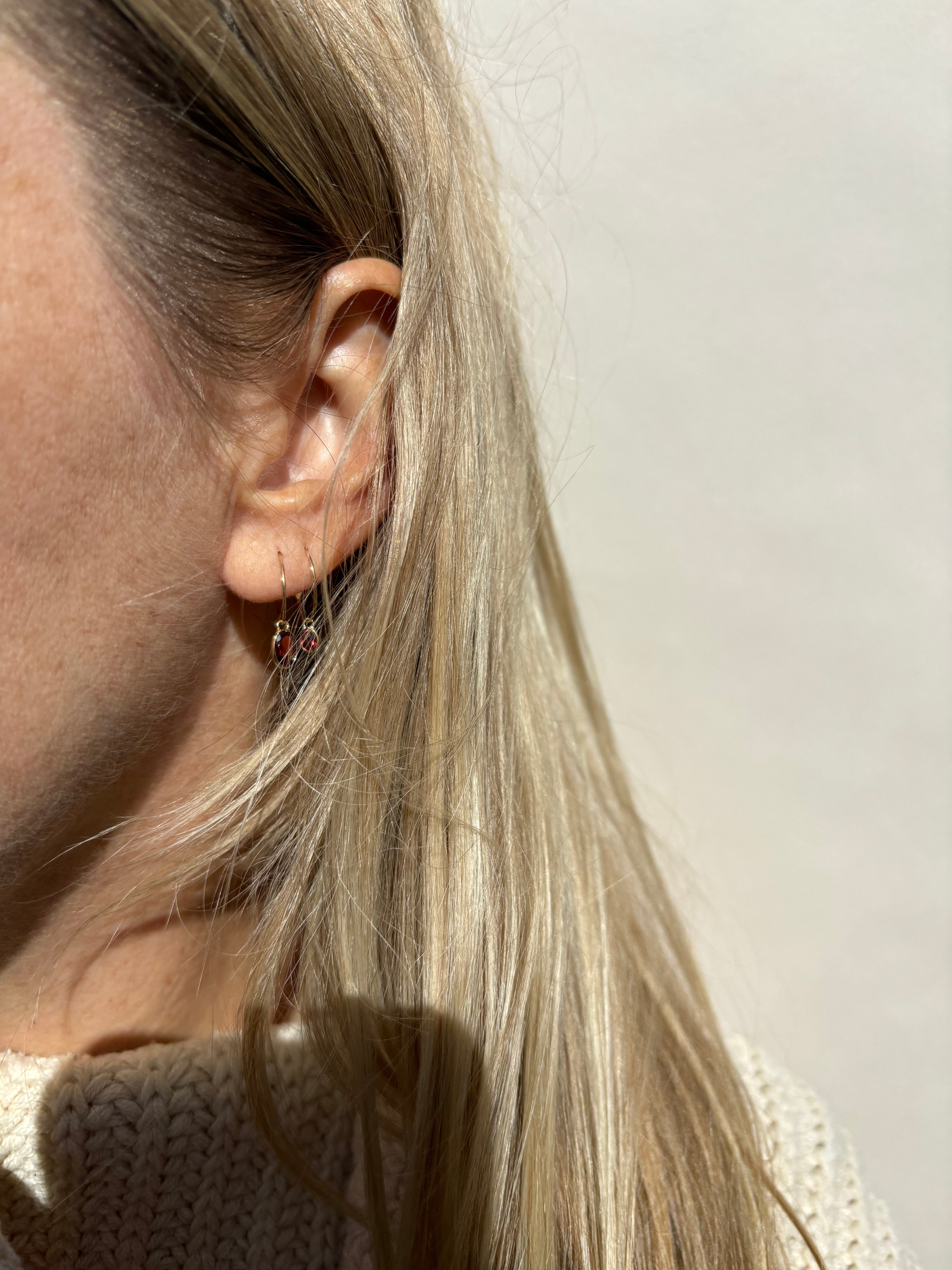 Model wearing Thalken 14k solid gold 10mm hoop with a small oval garnet drop in the second ear piercing, paired with a 12mm hoop featuring a medium oval garnet drop