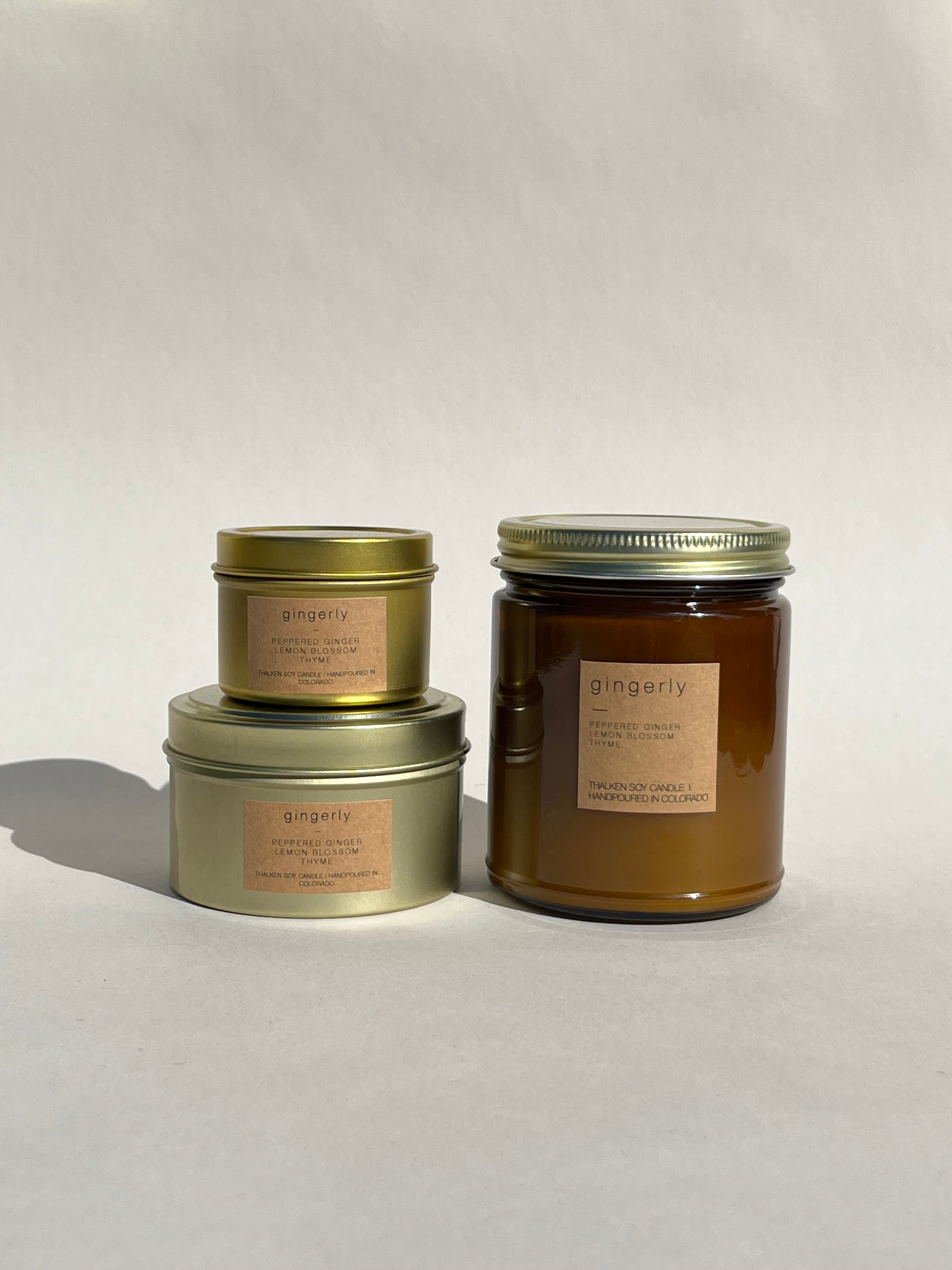 Thalken Gingerly candle in three containers — small gold tin, medium gold tin, and large brown glass jar — a spicy, sweet candle with notes of peppered ginger, lemon blossom, and thyme, reminiscent of ginger cake