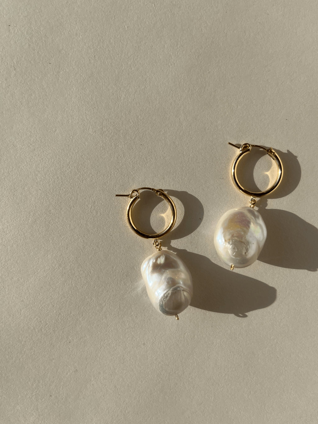Close-up of The Grand Freshwater Pearl Drops on a warm backdrop, featuring large freshwater pearls on gold-filled click hoops