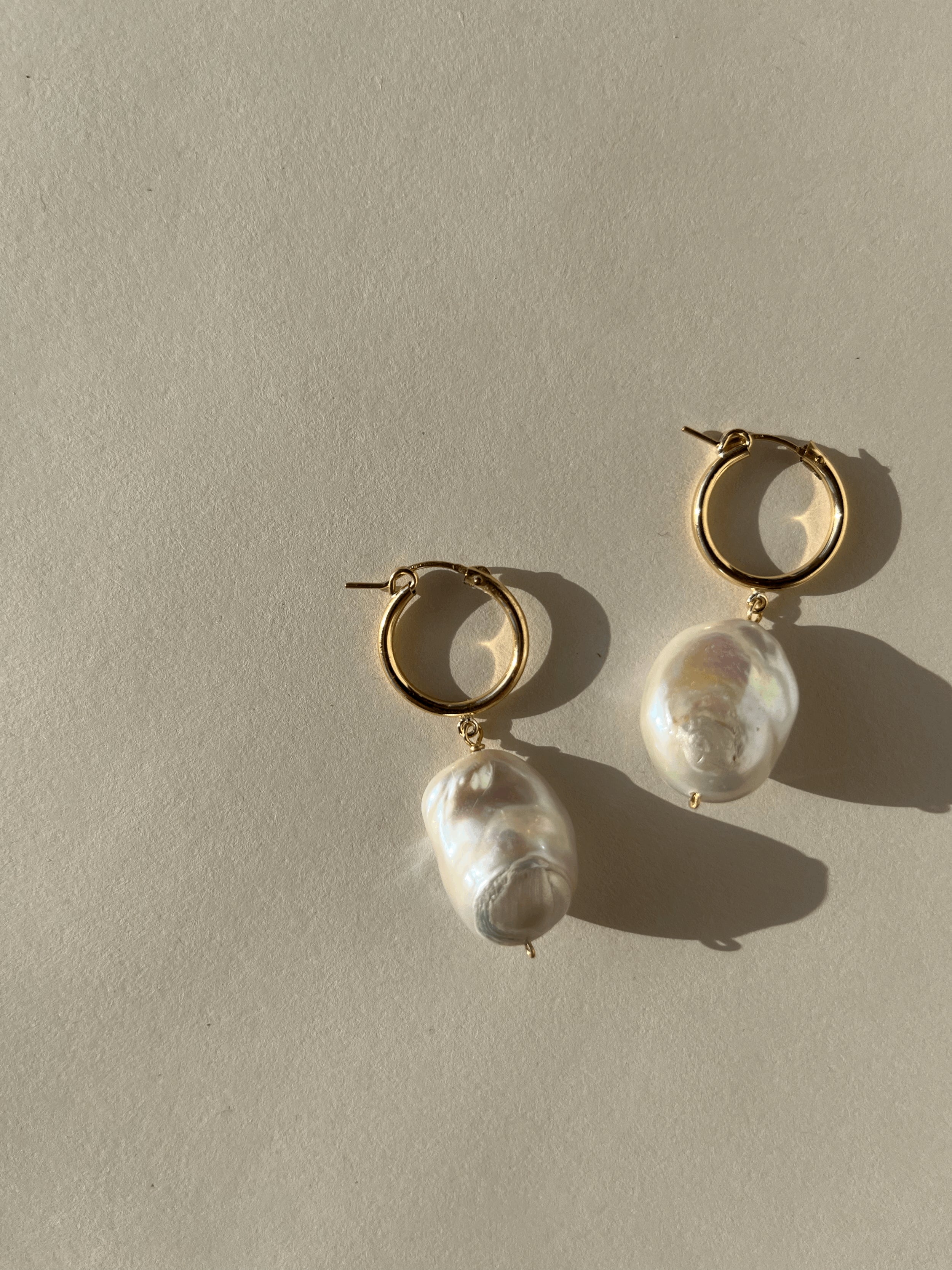 Close-up of The Grand Freshwater Pearl Drops on a warm backdrop, featuring large freshwater pearls on gold-filled click hoops