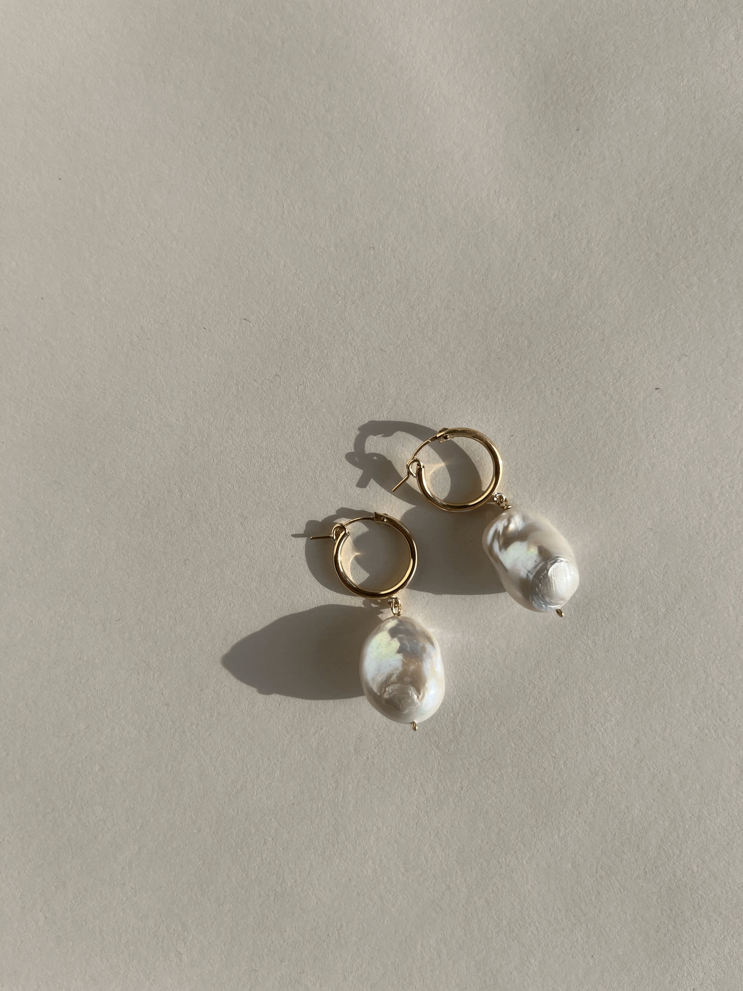 The Grand Freshwater Pearl Drops displayed on a warm backdrop, showcasing their elegant gold-filled hoops and statement pearls