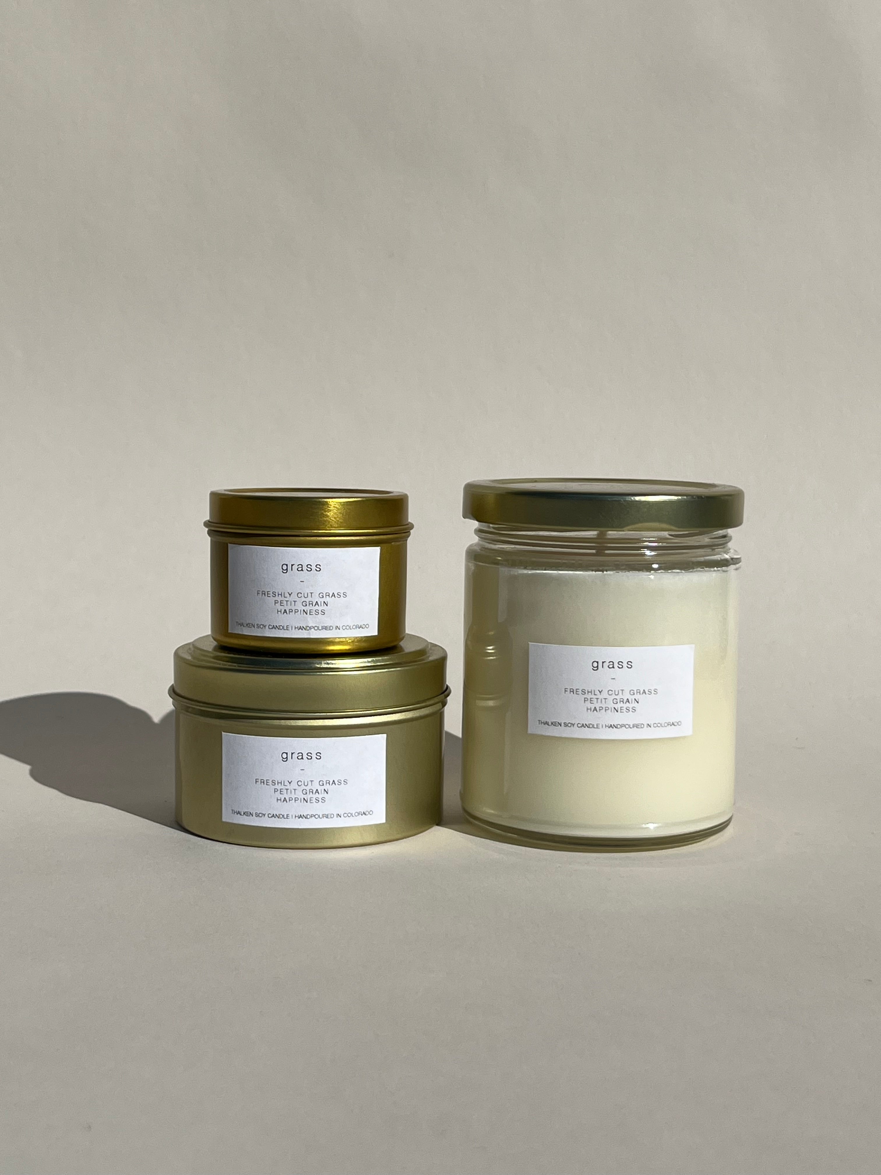 Thalken® Grass candles in three sizes — 2oz and 6oz gold tins and 8oz soft-glow glass jar. Scent profile: bright and fresh with notes of freshly cut grass, grapefruit, and petit grain
