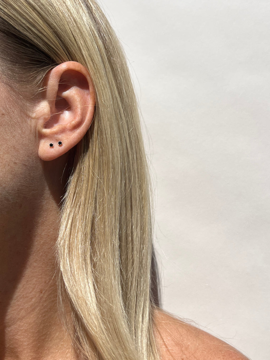 Model wearing the black Itty Bitty Crystal Stud earrings in sterling silver in her first and second ear piercings, styled for a minimalist layered look