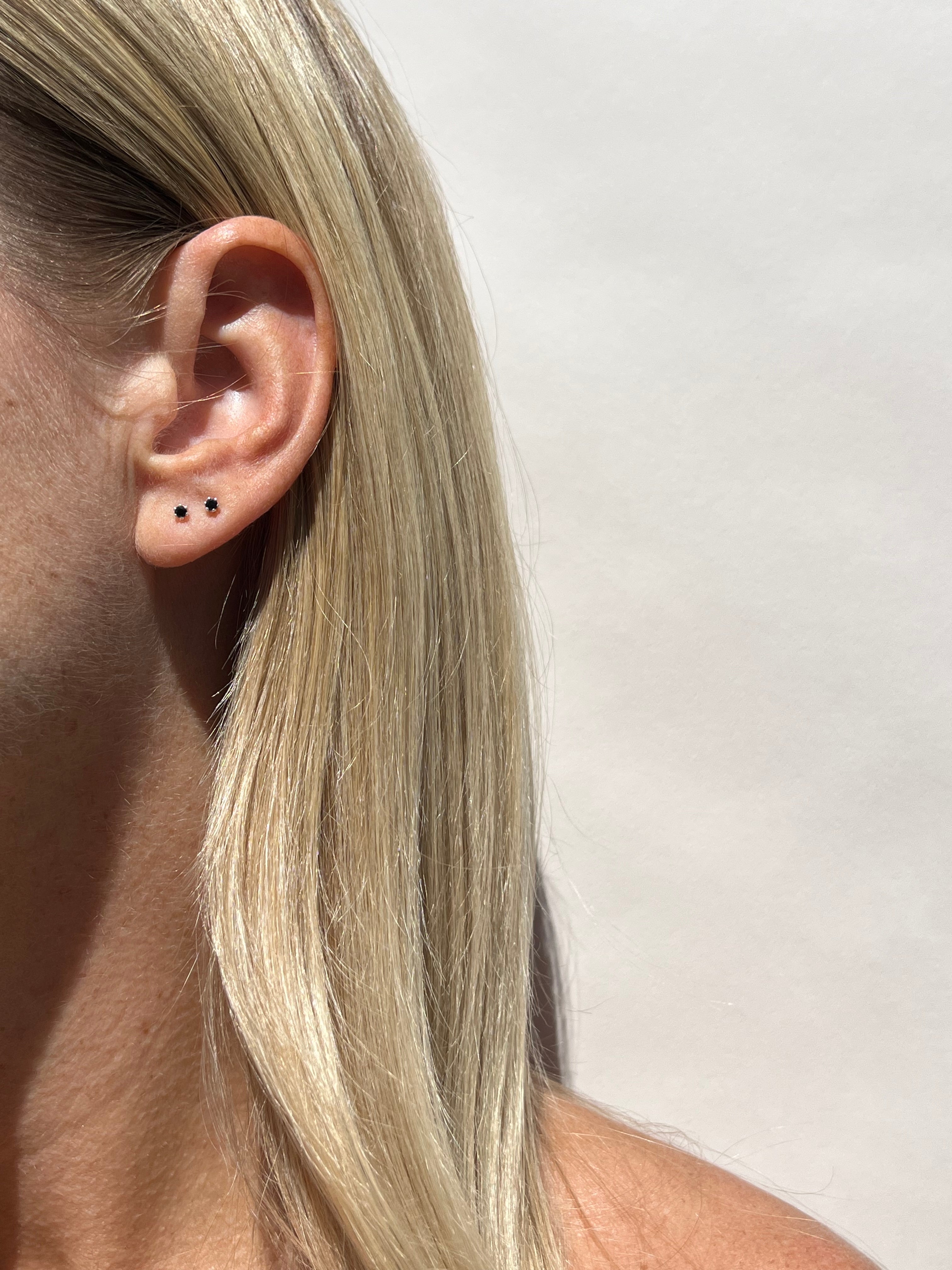 Model wearing the black Itty Bitty Crystal Stud earrings in sterling silver in her first and second ear piercings, styled for a minimalist layered look