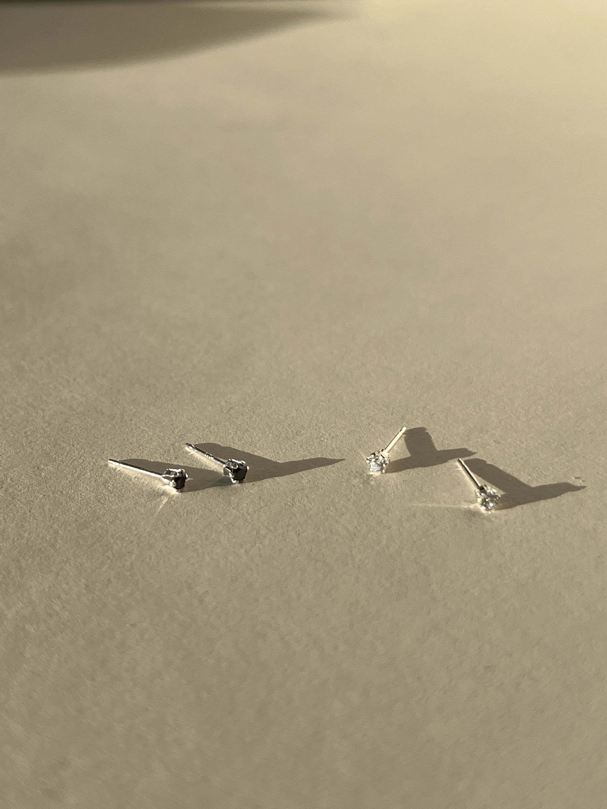 Two pairs of tiny Itty Bitty Crystal Stud earrings in sterling silver, shown in black cubic zirconia and clear cubic zirconia side by side on a neutral background