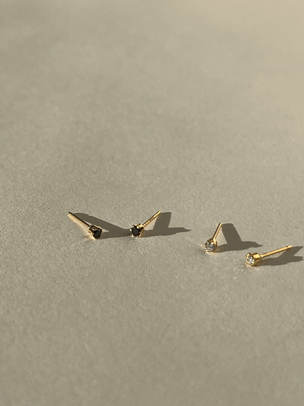 Distant shot of two pairs of tiny yellow gold-filled cubic zirconia stud earrings, featuring one black pair and one clear pair, styled for minimalist everyday wear