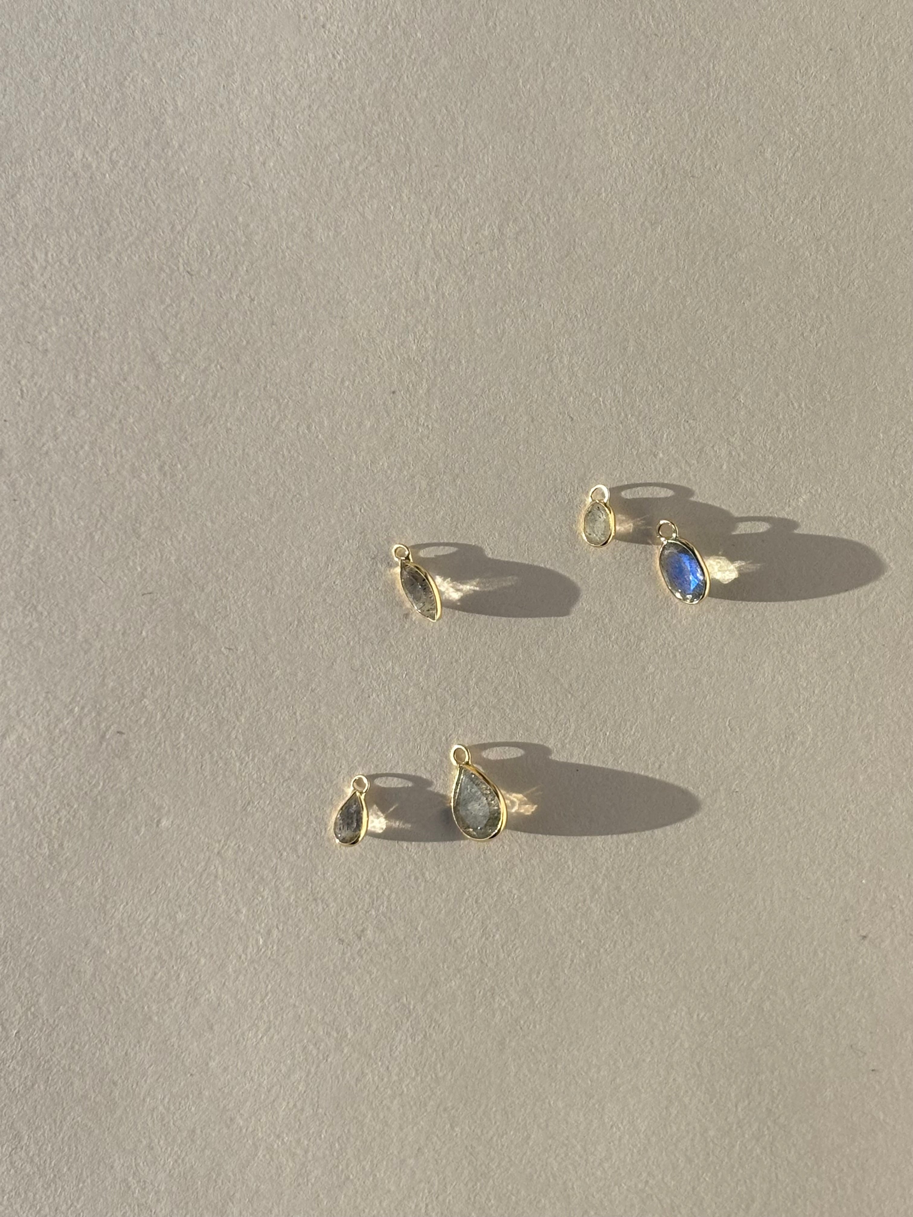 Assorted Thalken 14k gold single drop earring charms in pear, marquise, and oval shapes, displayed unattached to 10mm and 12mm hoop earrings for custom styling options