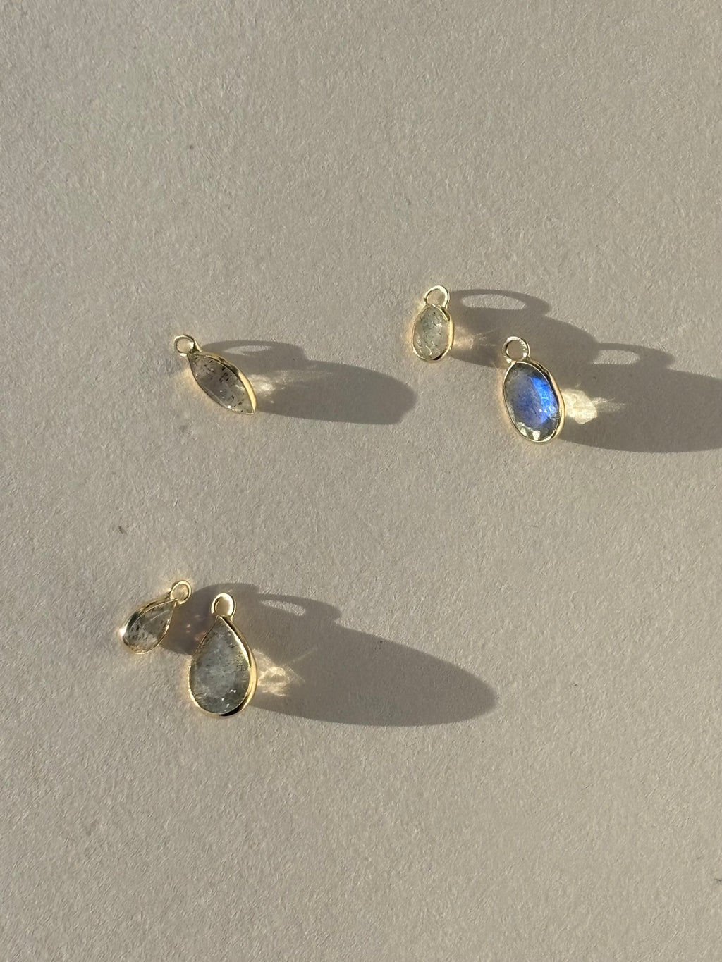 Close-up of assorted Thalken 14k gold single drop earring charms in pear, marquise, and oval shapes, displayed unattached to 10mm and 12mm hoop earrings for custom styling options