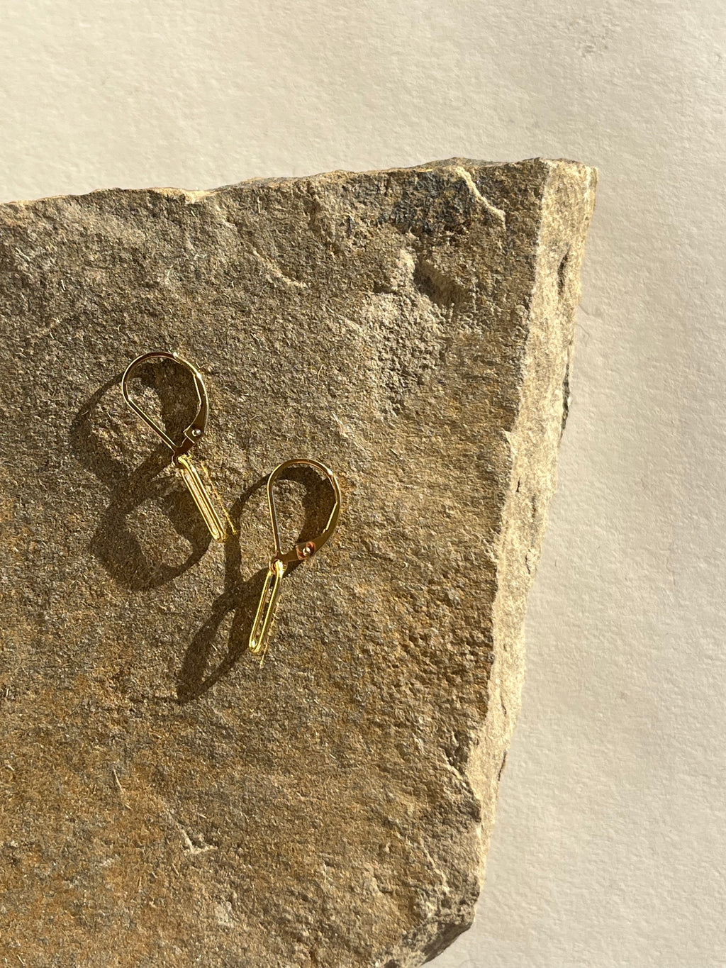 Large paperclip leverback earrings in yellow gold-filled displayed on a textured rock surface, highlighting their modern shape and warm gold tone