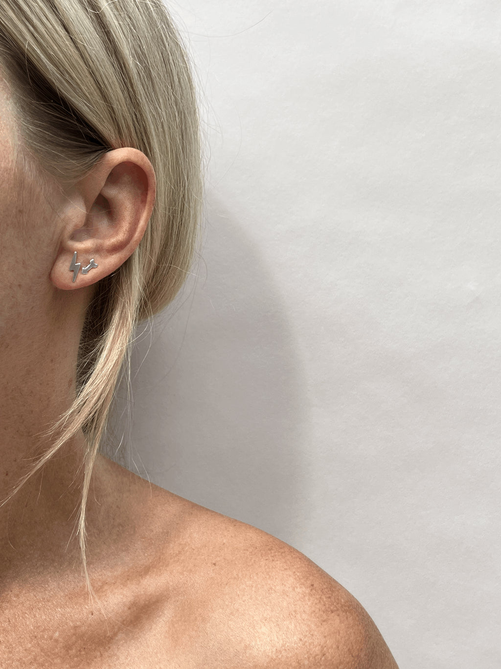 Model wearing a sterling silver lightning bolt stud earring in her first ear piercing and an arrow stud earring in her second ear piercing, different angle